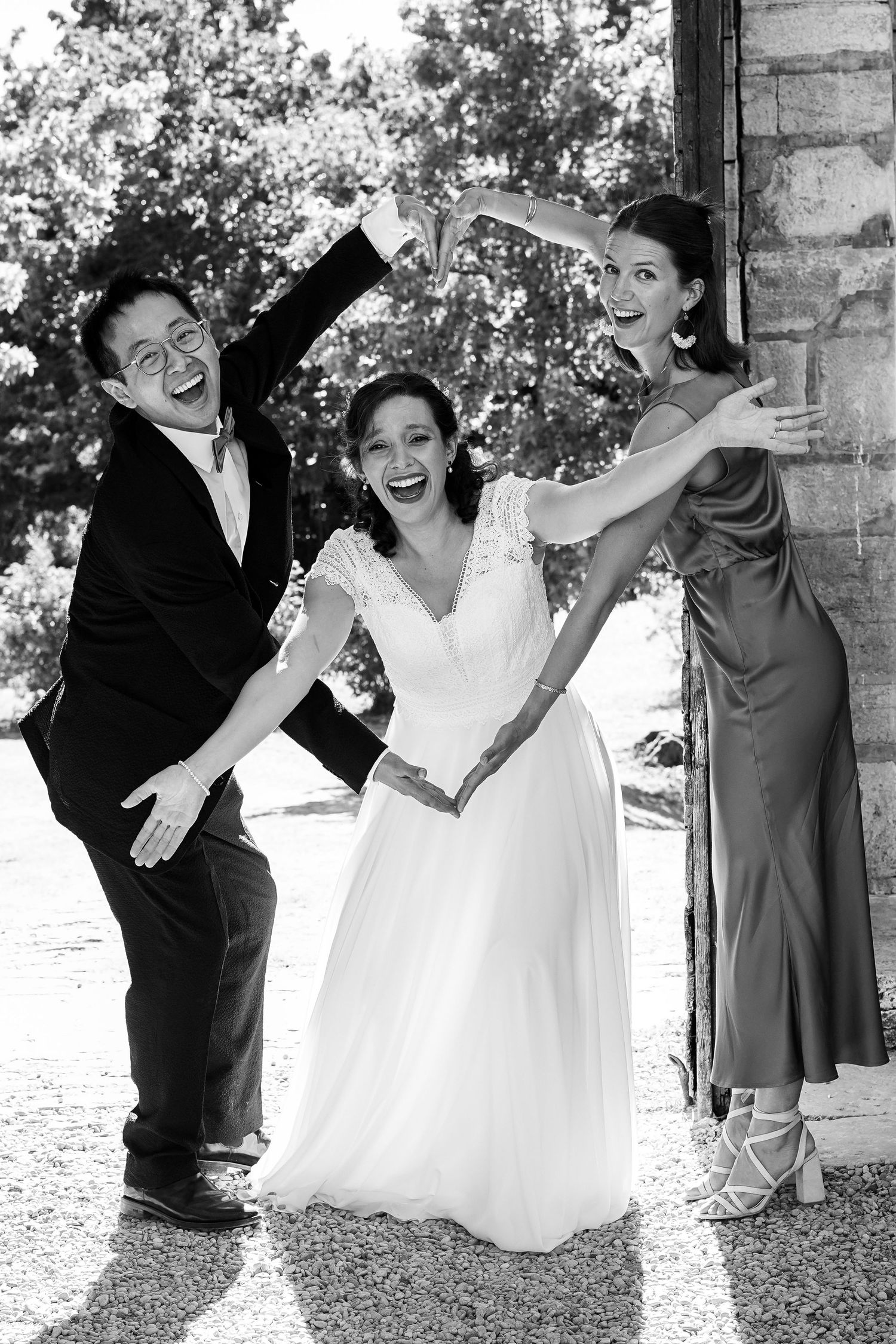 Joyful black and white photo of bride posing with two laughing wedding guests outside.