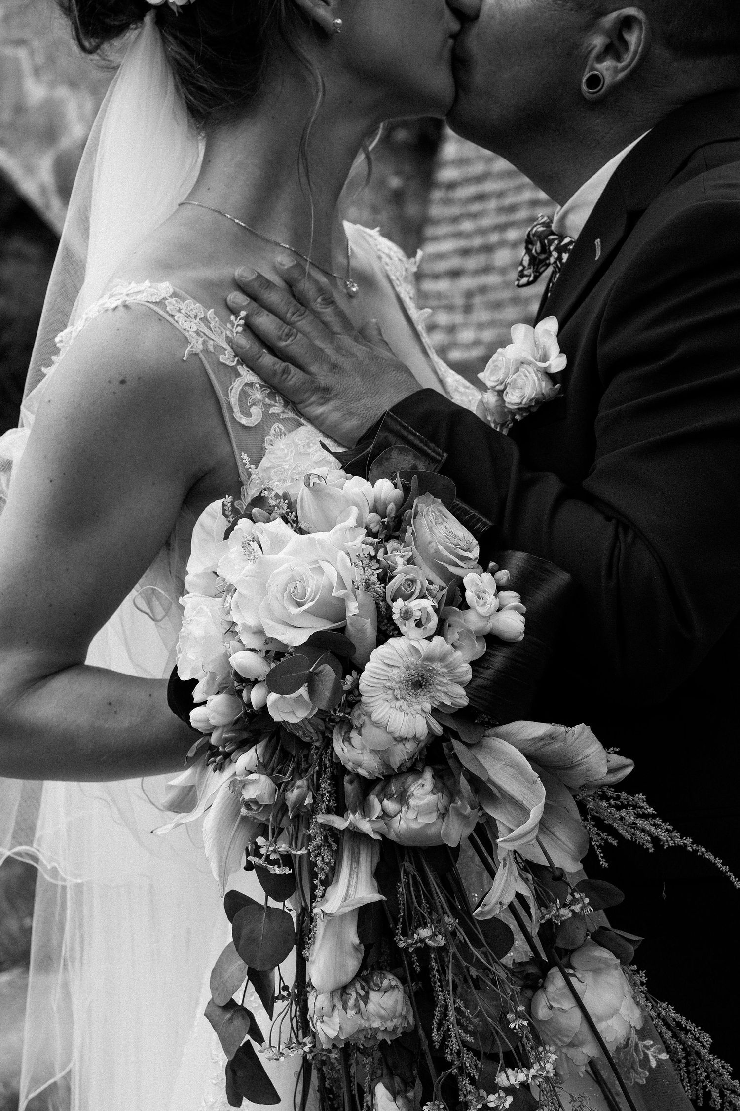 Black and white photo of bride and groom kissing, bride holding a lush floral bouquet.