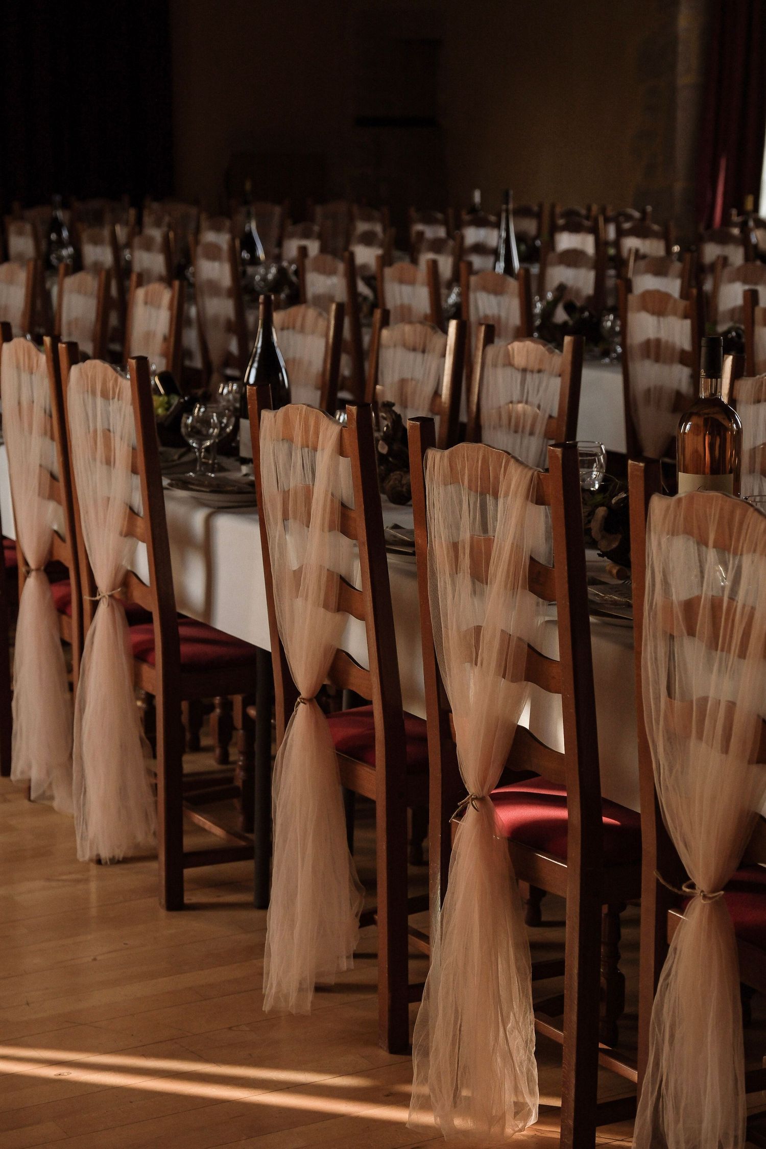 Elegant wedding reception hall with rows of wooden chairs adorned with white tulle ribbon decor.
