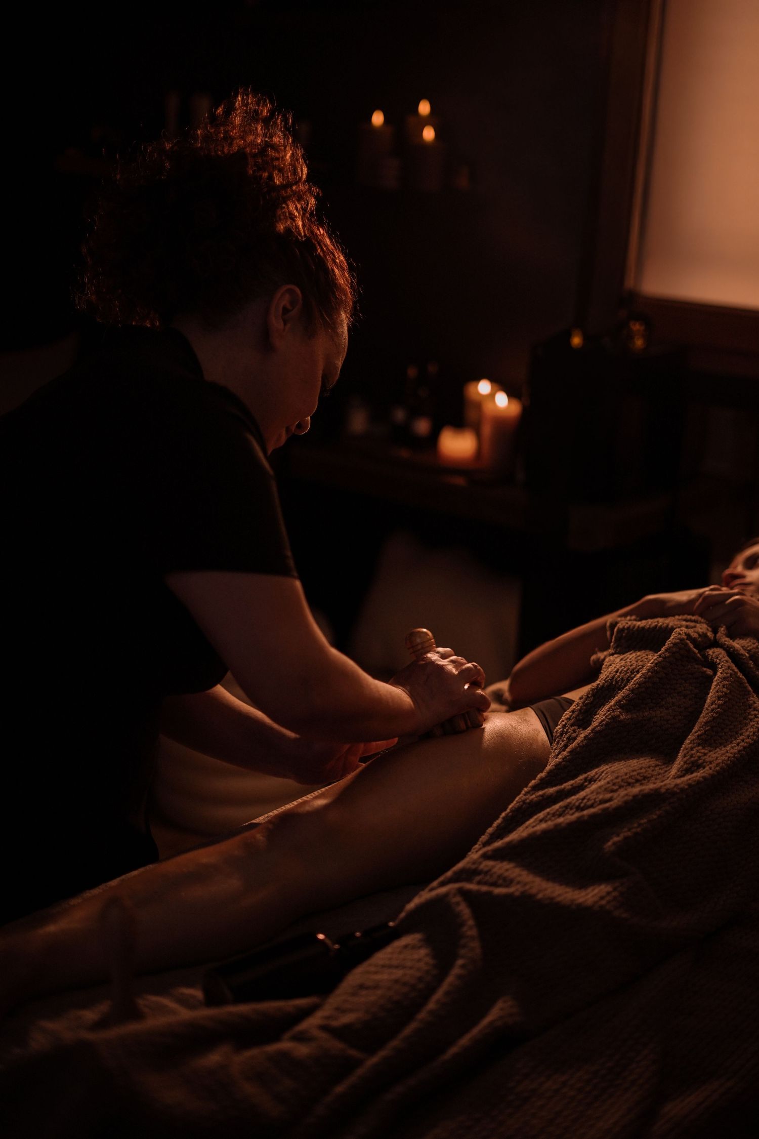 Massage therapist performing relaxing foot massage by candlelight in dark spa setting.