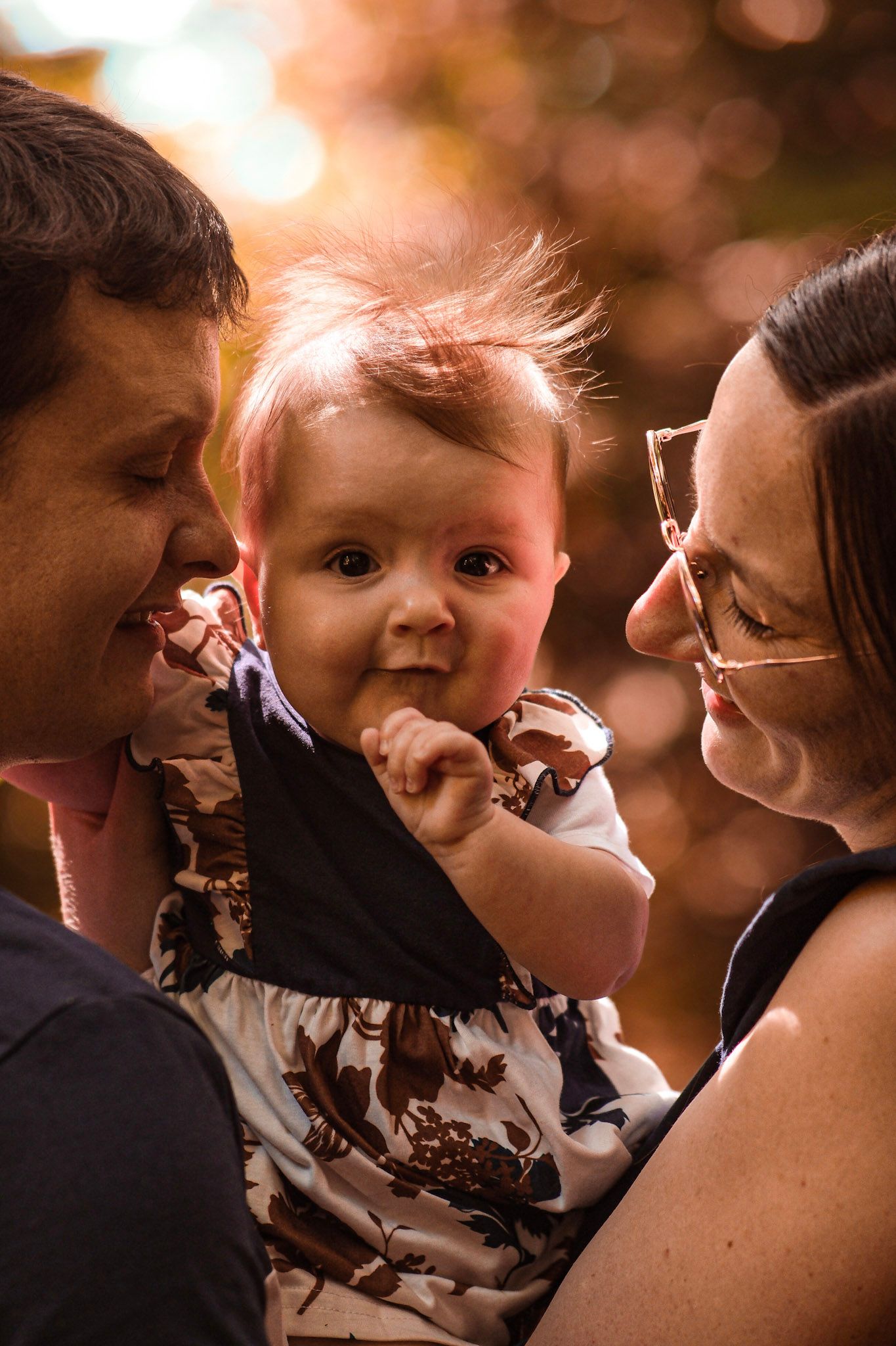 Happy parents smiling at their baby in warm autumn sunset light outdoors.