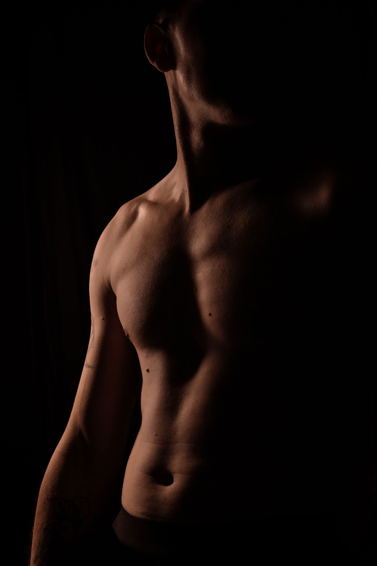 Athletic male torso with defined abs and muscles against dark black background.