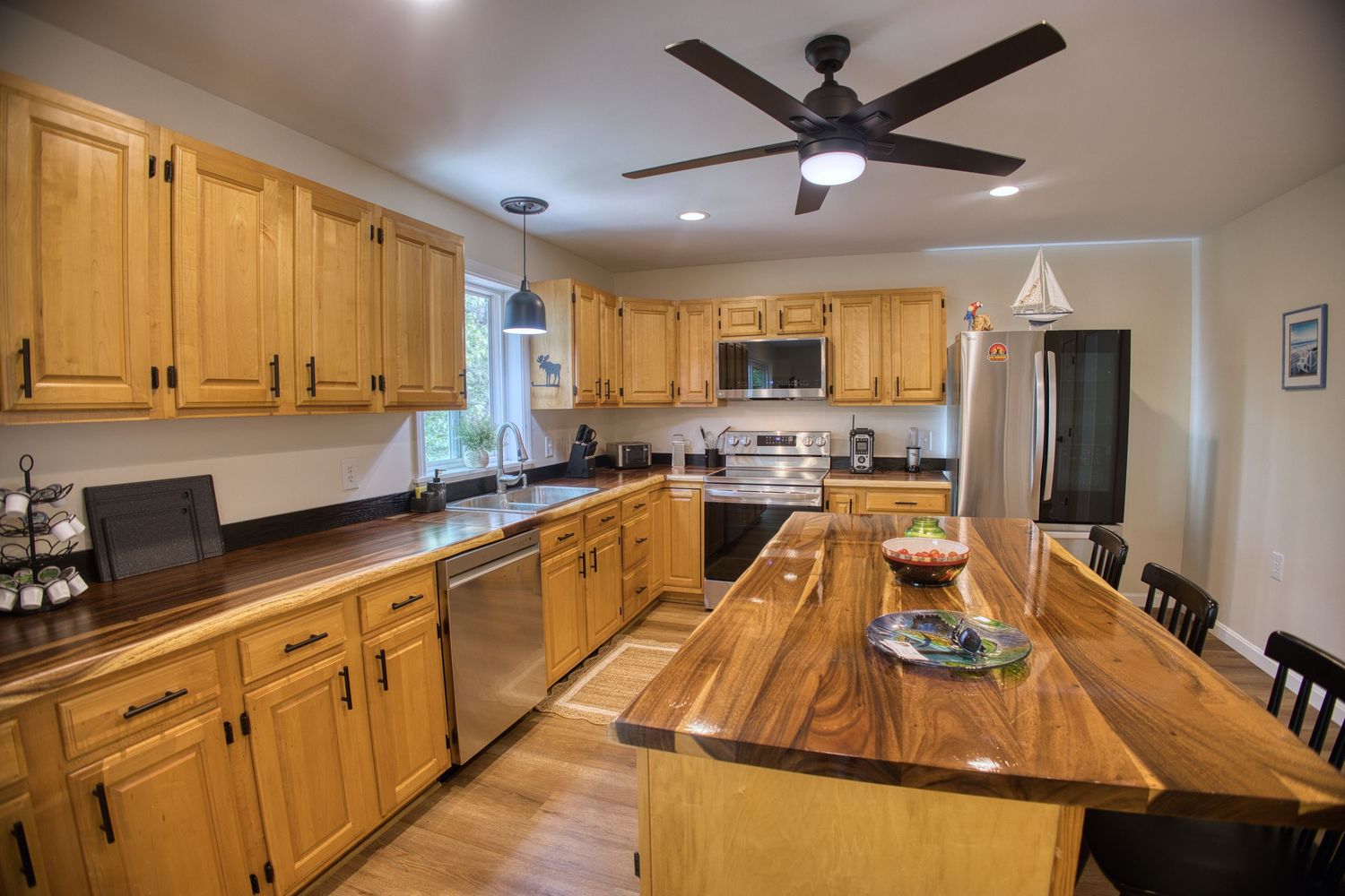 Modern kitchen with honey oak cabinets, black appliances, and ceiling fan features multiple vantage points.