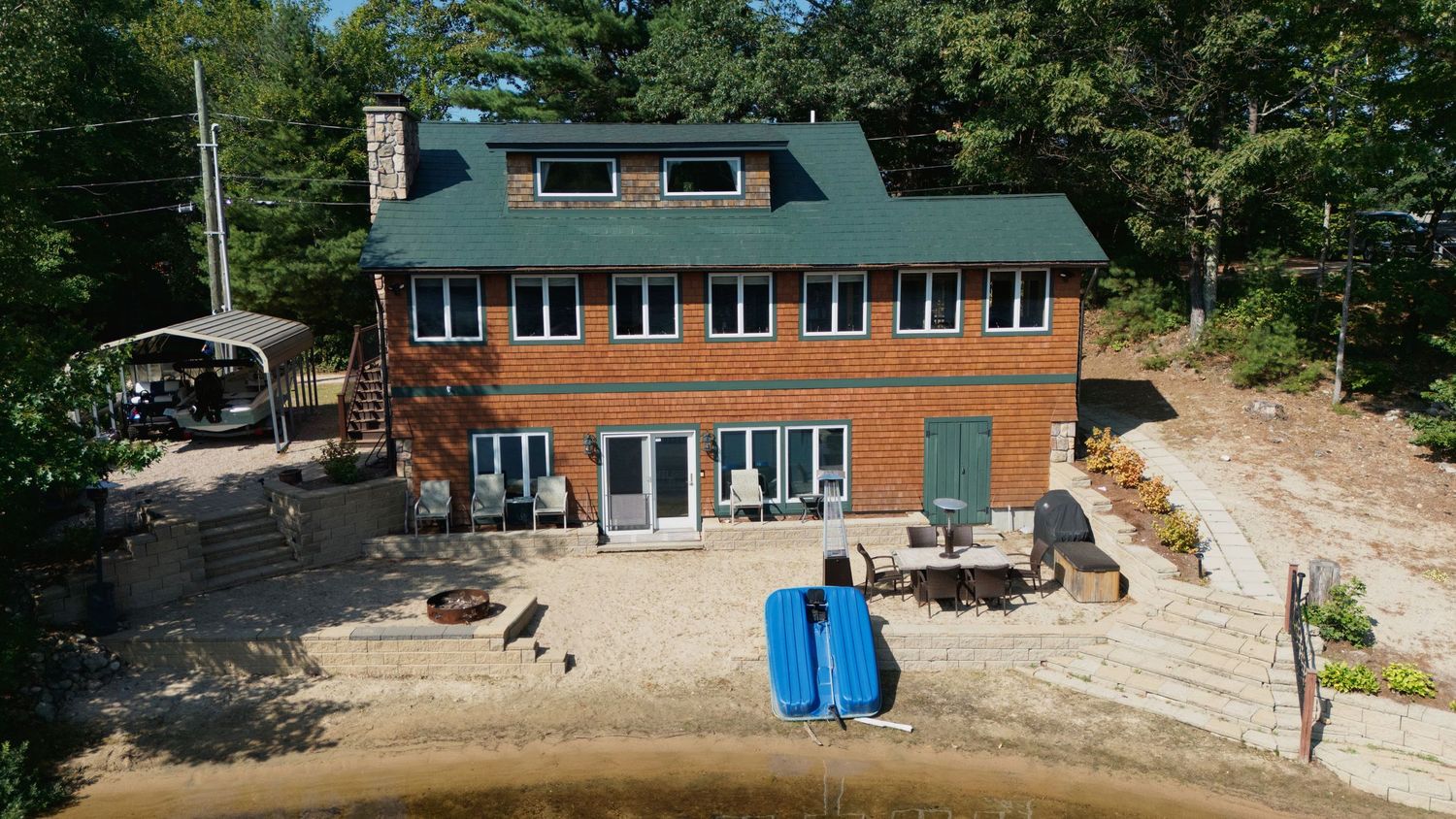 A panoramic view of a lakefront residential property with green trees and landscaping surrounding the home.