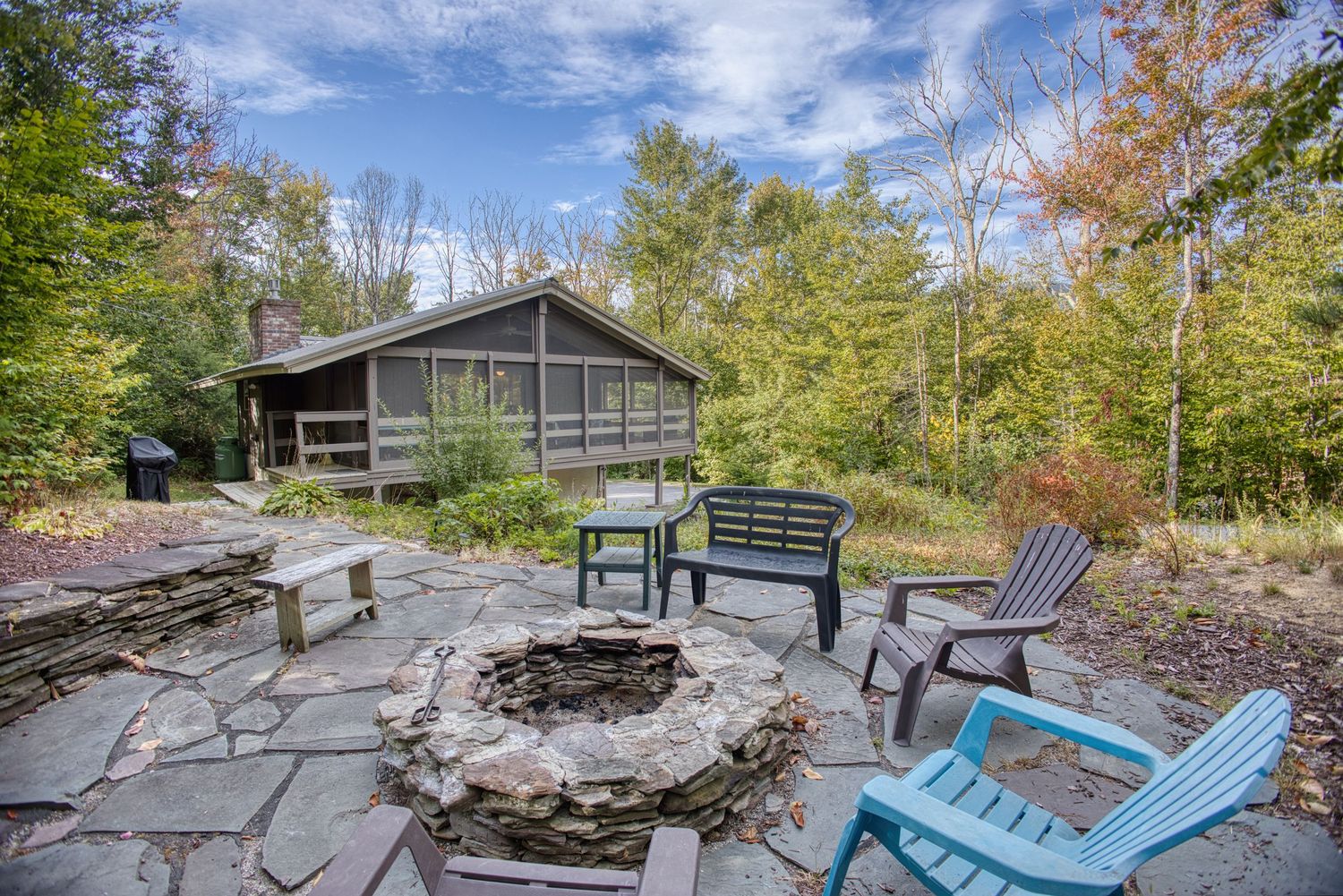 A rustic mountain cabin deck with Adirondack chairs overlooking scenic forest views on a sunny autumn day.