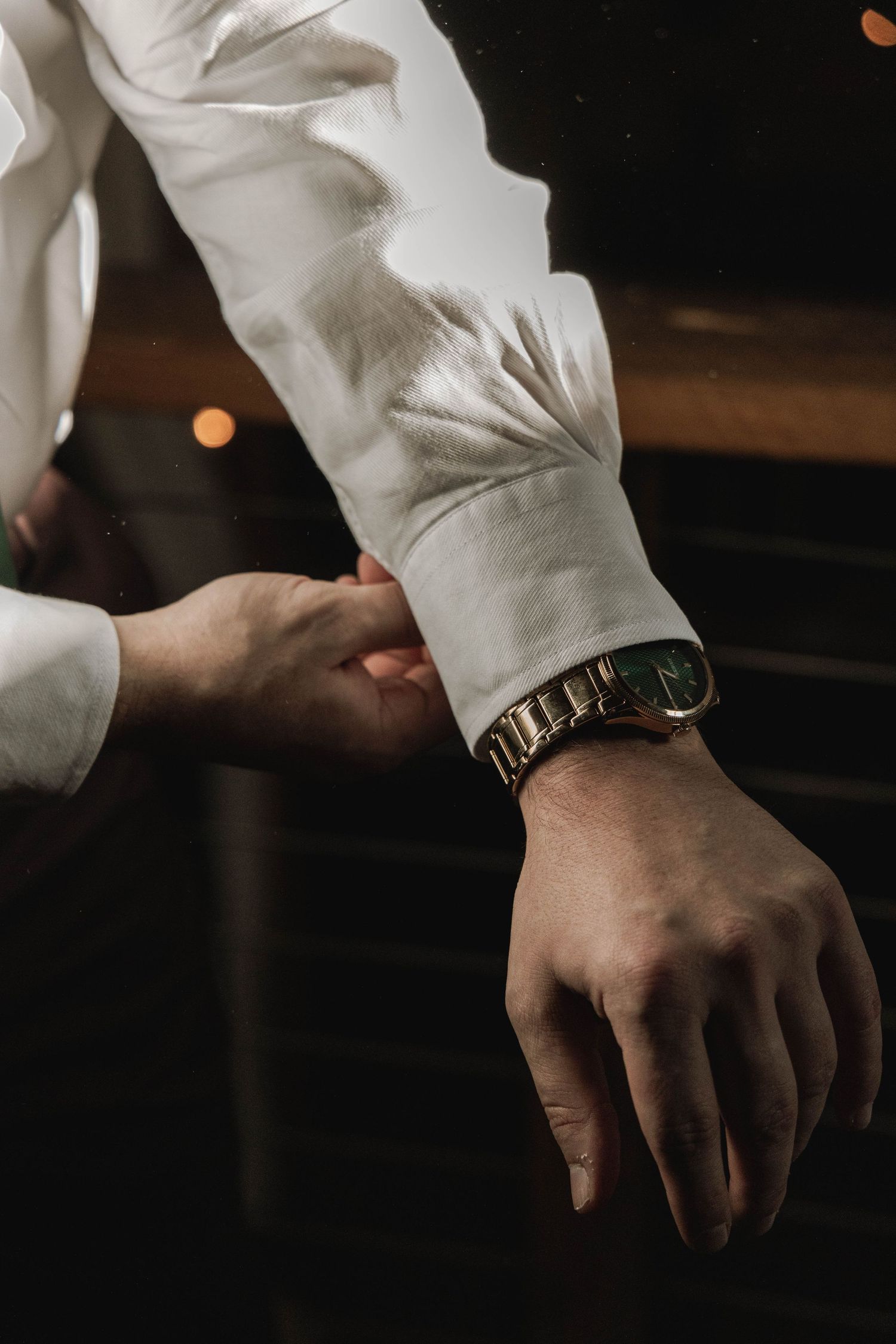 Elegant silver watch worn on wrist with crisp white dress shirt sleeve in moody lighting.