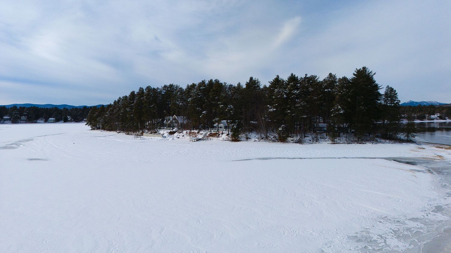 Panoramic winter landscape view of a snow-covered lake surrounded by evergreen forest and mountains.