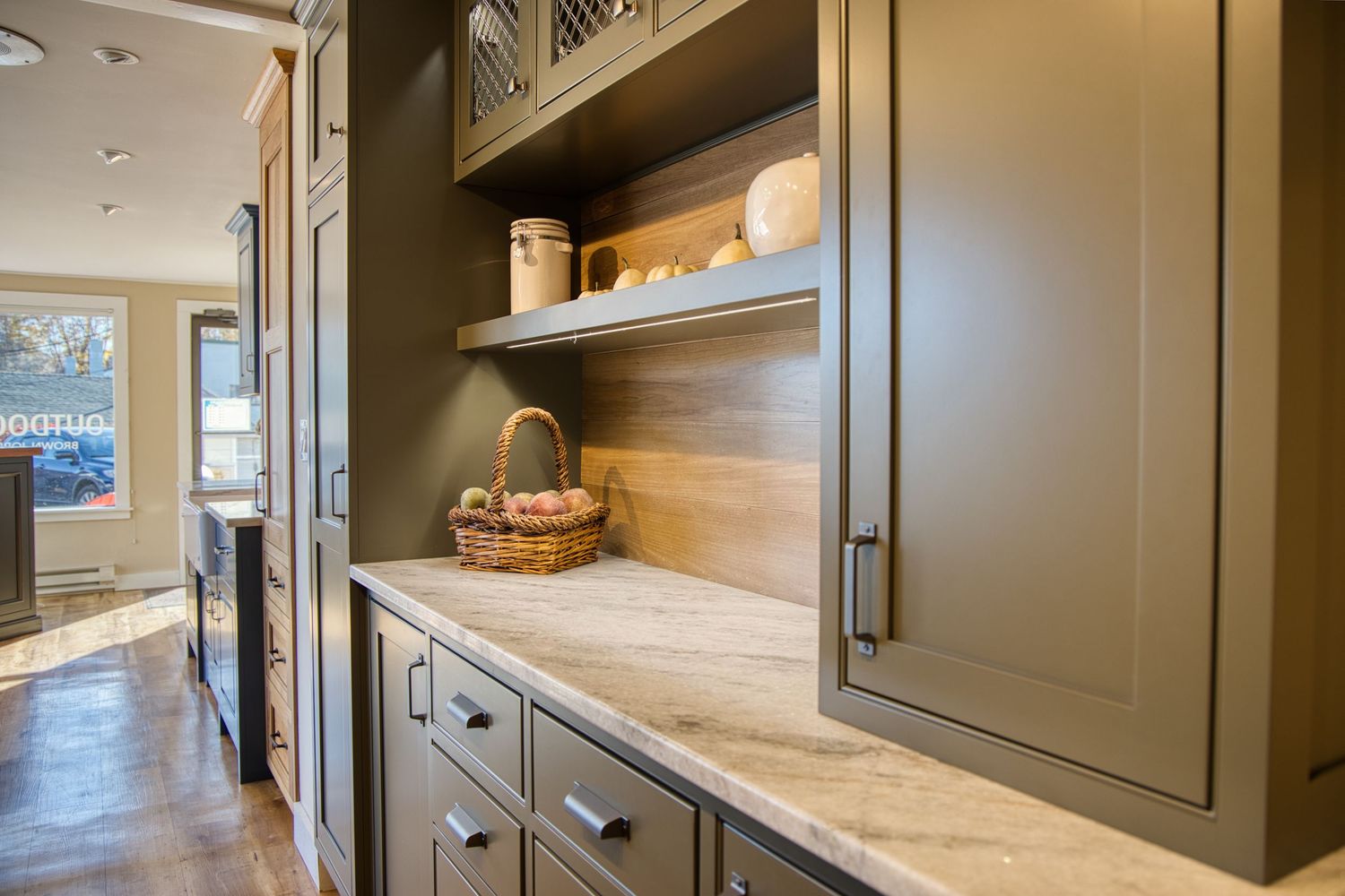Modern butler's pantry with olive green cabinets, marble countertops, and wood backsplash features built-in storage.