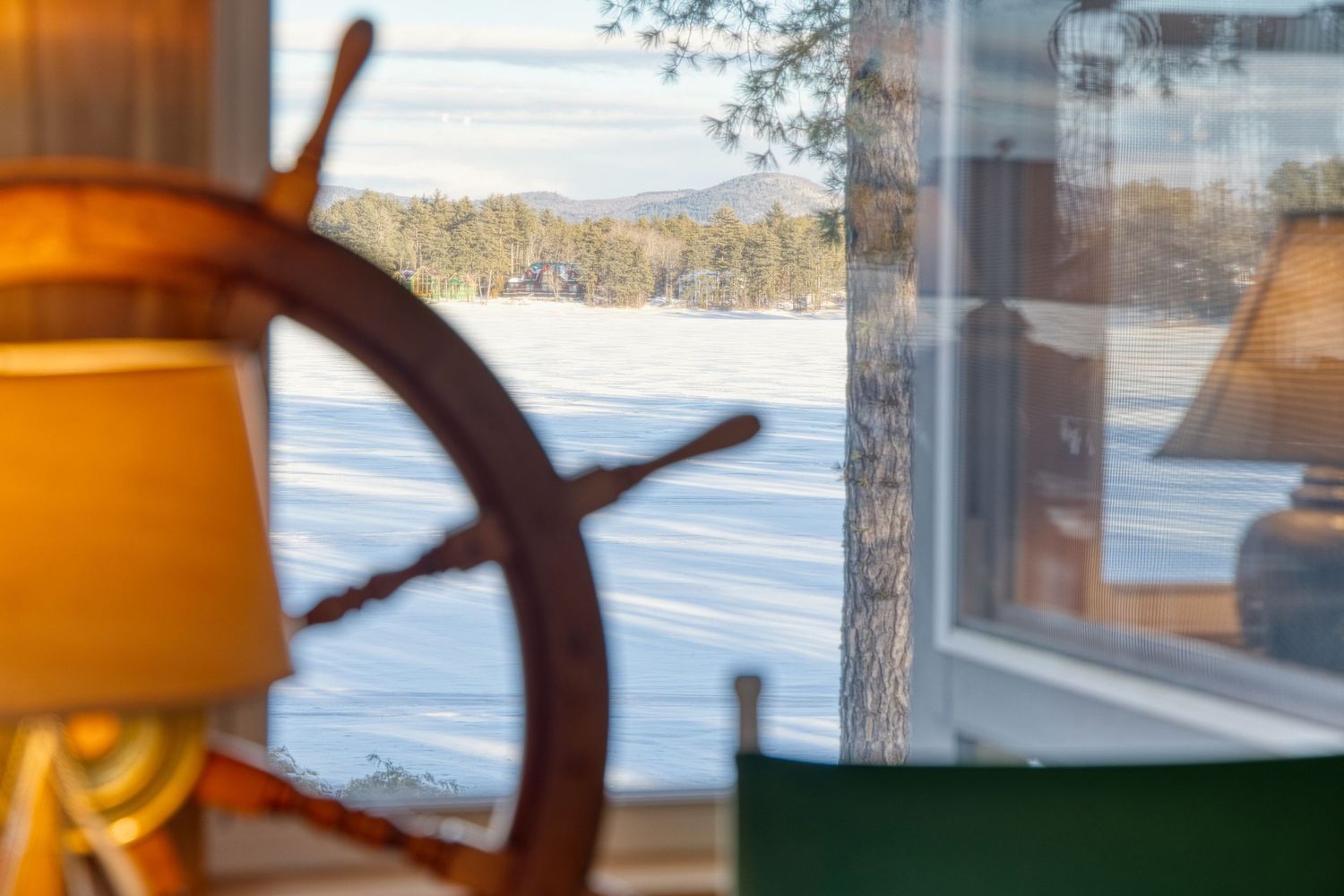 Orange sunset light streams through windows overlooking a snowy winter landscape with trees and a frozen lake.