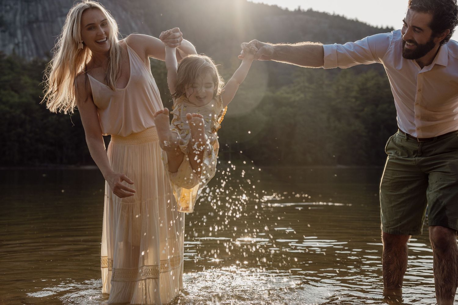 Couple splashing and playing together in a sunlit lake during a romantic summer photoshoot.