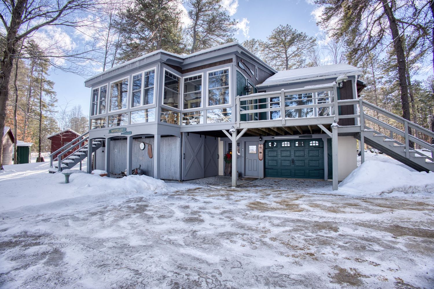 Snow covered property with multiple buildings and tall pine trees visible in winter landscape.