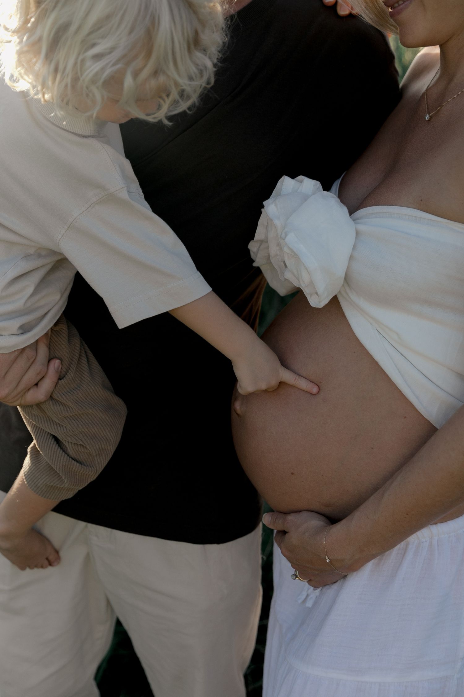 Young child pointing at pregnant mothers bare belly outdoors in natural light.