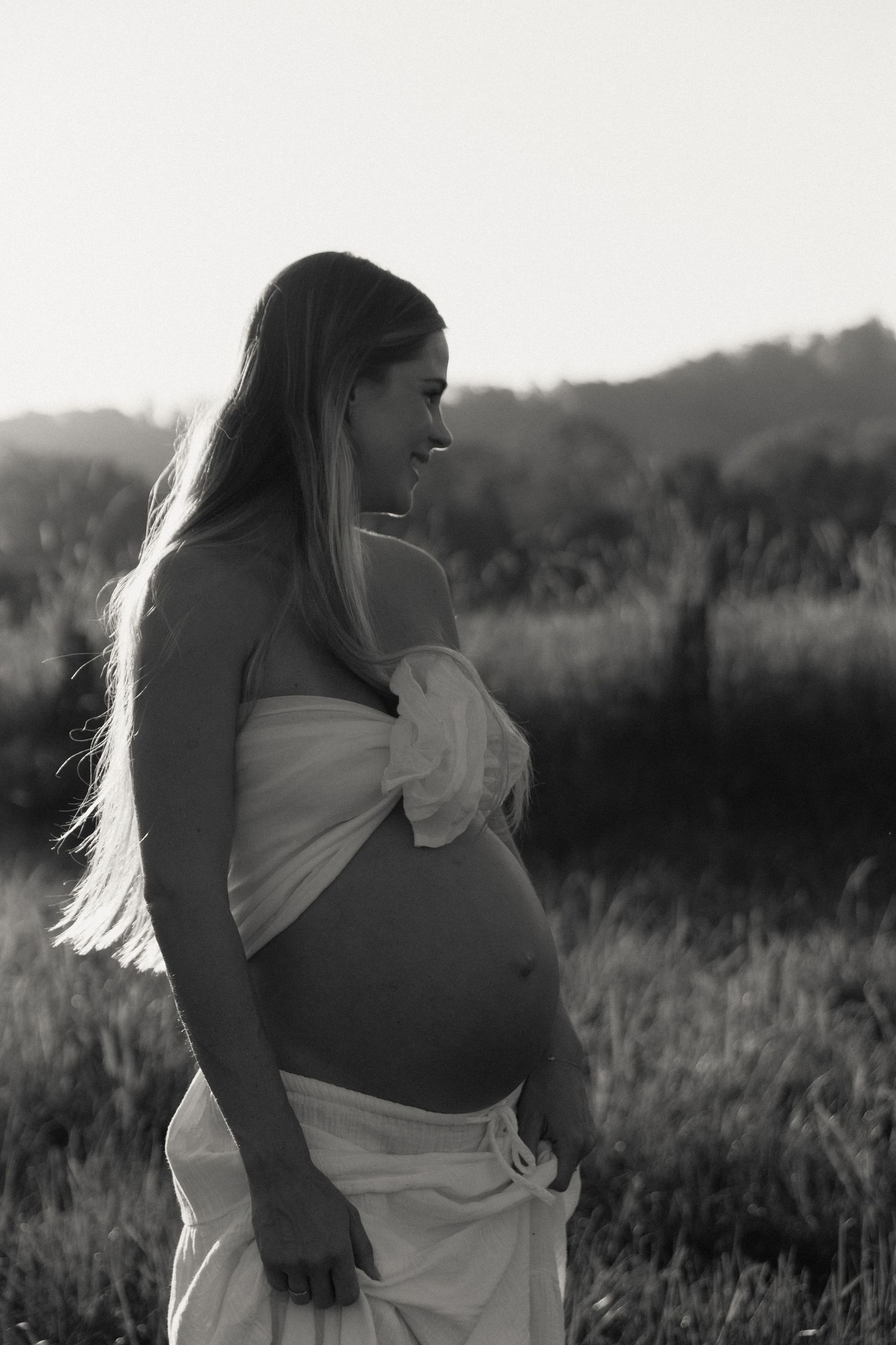 Black and white portrait of smiling pregnant woman in white wrap outdoors.