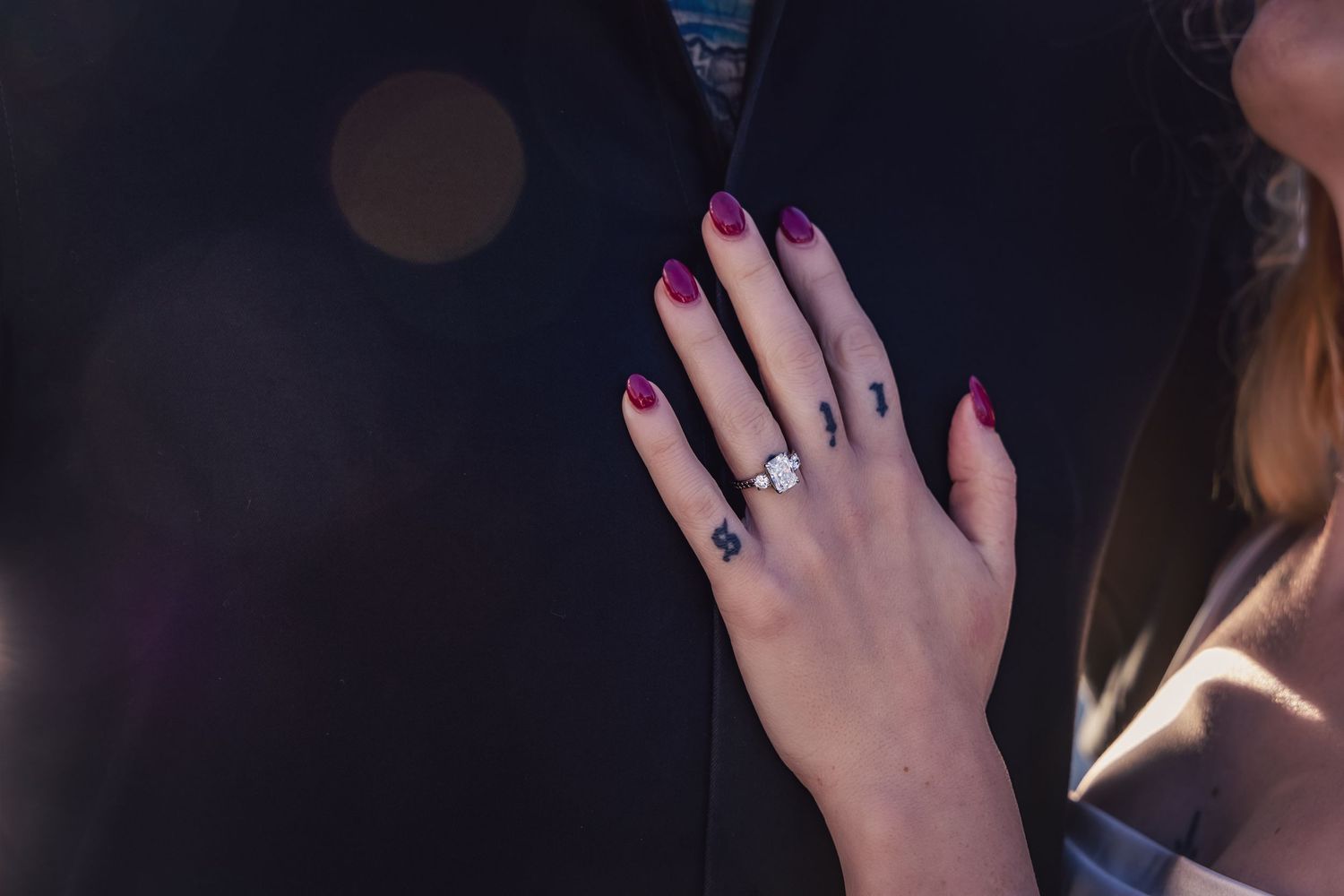Close-up view of a hand with pink nail polish wearing multiple decorative rings against a dark background.