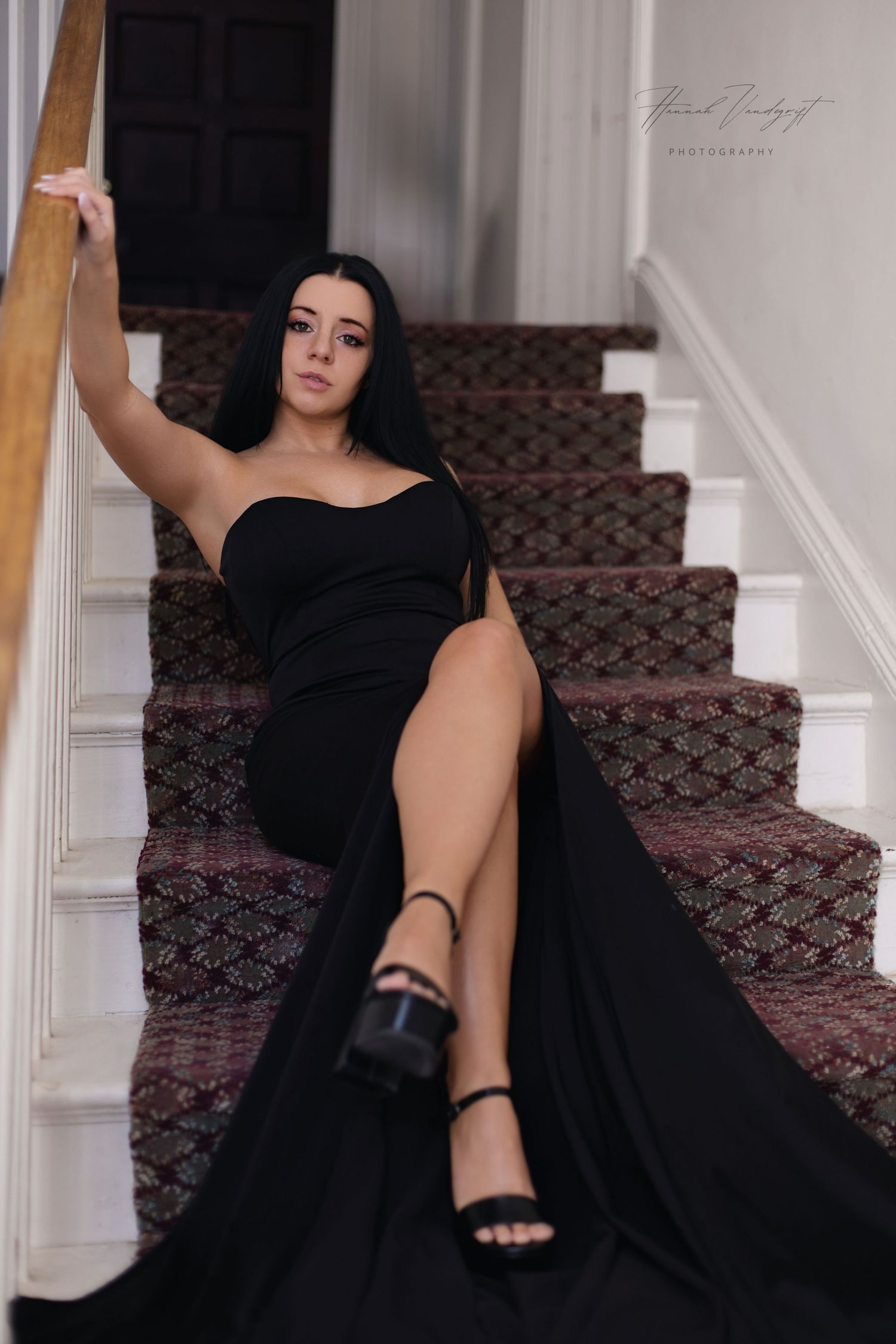 Elegant figure in black dress poses dramatically on carpeted staircase.