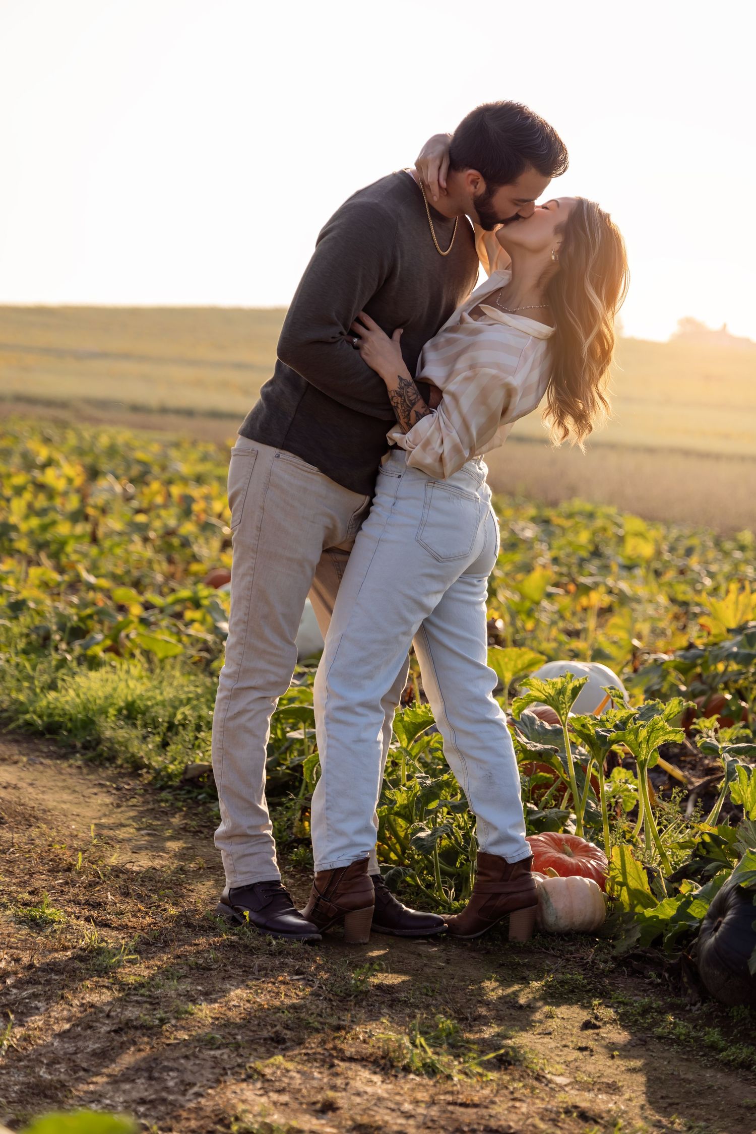 A couple embraces while standing in a sunflower field at sunset creating romantic silhouettes against golden light.