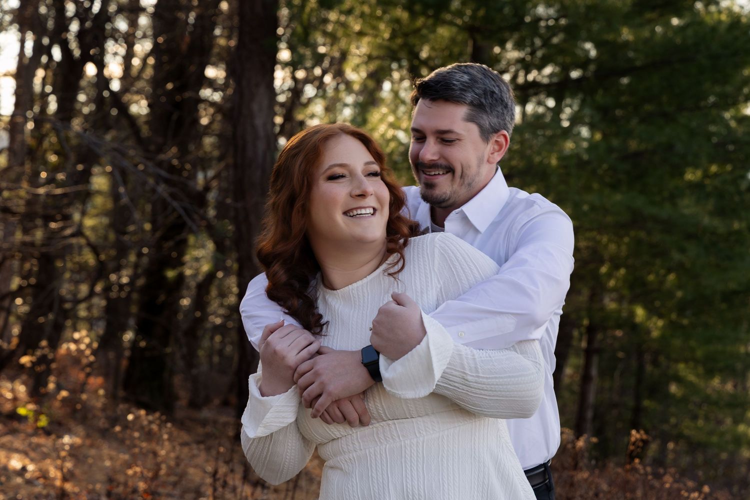 A couple shares a romantic moment outdoors in a wooded area during an engagement photo session.
