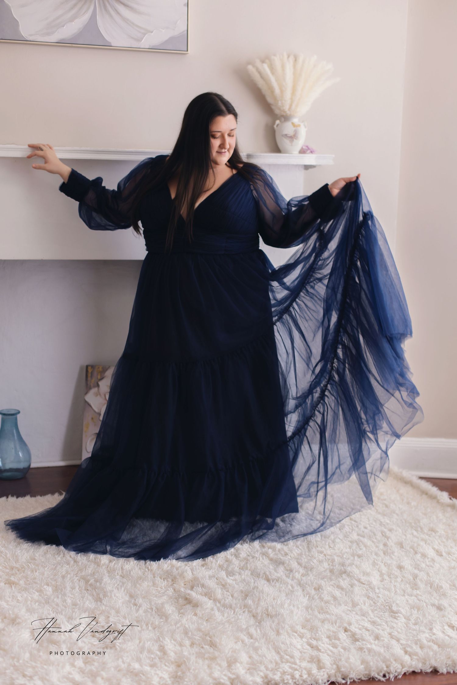 Flowing navy blue evening gown with sheer sleeves photographed against light interior backdrop.