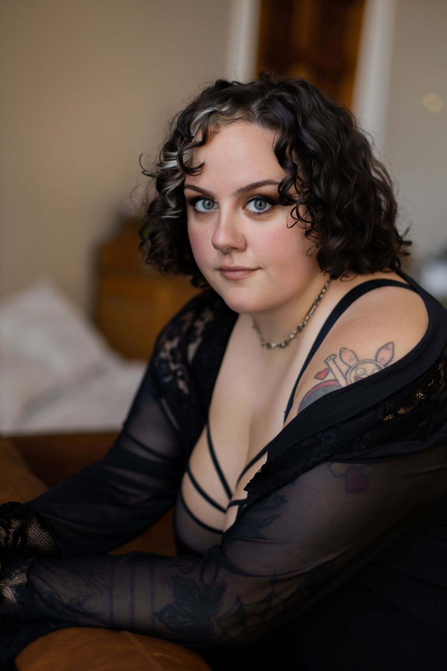 A plus size model in black sheer clothing poses seductively on a couch during a boudoir photo session.