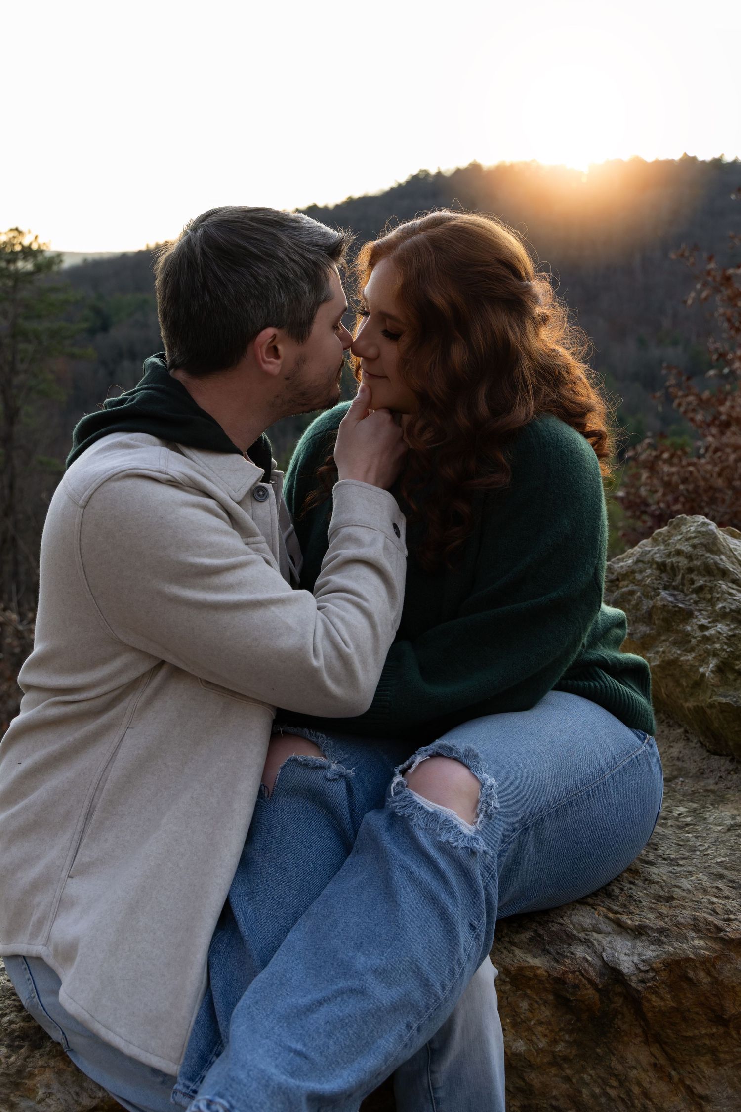 A couple sits together on a rocky overlook at sunset sharing an intimate moment in nature.