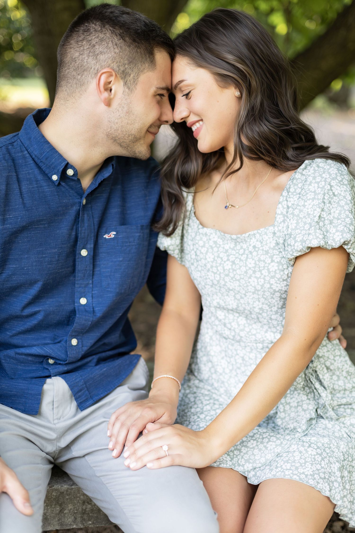 A tender moment shared between a couple in coordinated blue and white outfits under green trees.