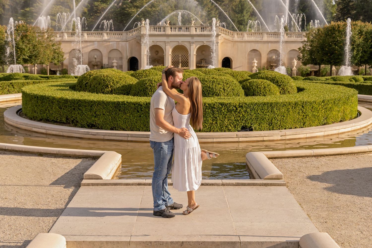 Romantic couple takes sunset wedding photos in an elegant Mediterranean garden courtyard with ornate fountains and manicured hedges.