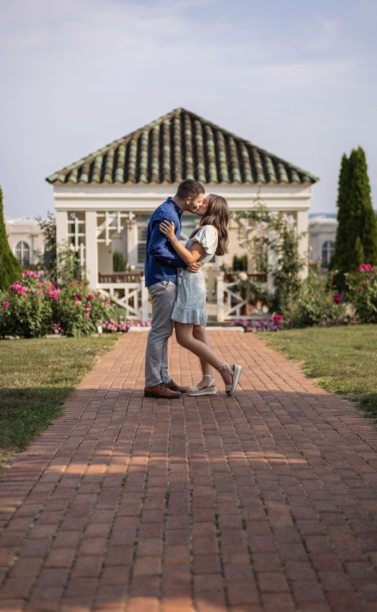 A romantic proposal sequence on a brick pathway with garden and architectural elements in the background.