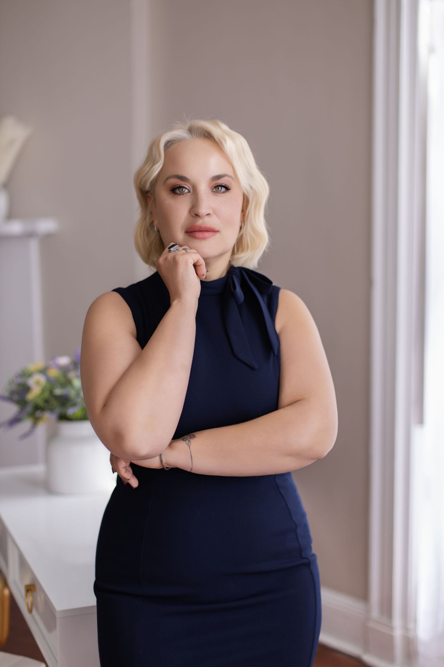 Professional portrait of woman in navy dress against light interior background.