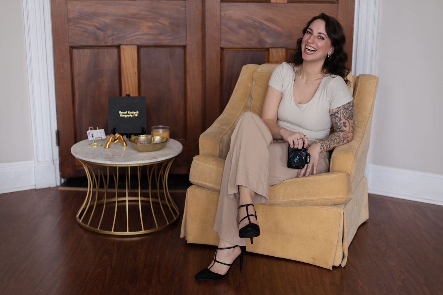 Model relaxes in tan armchair beside small table with refreshments.