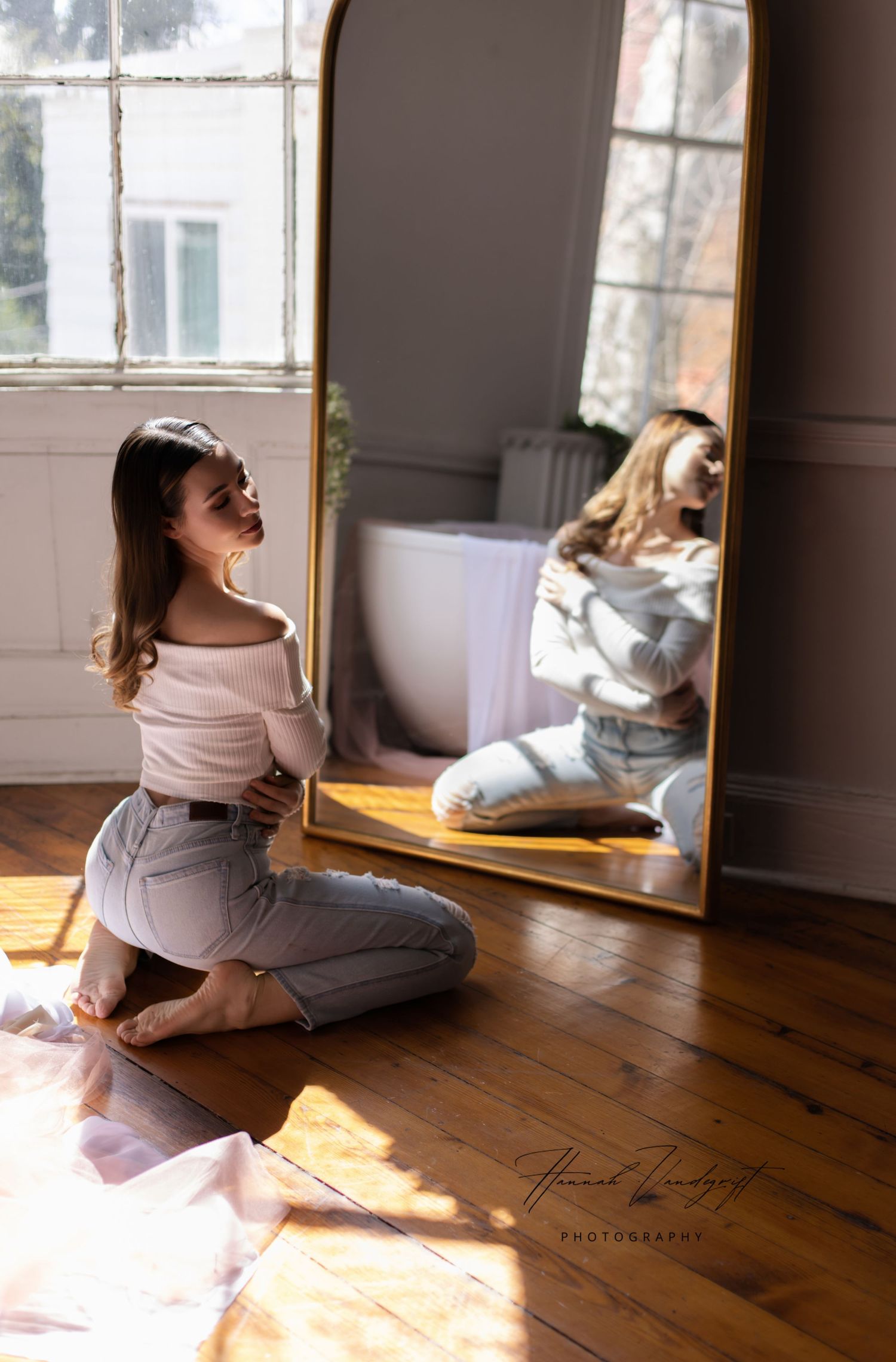 Person in cozy white sweater relaxes on hardwood floor in sunlit room.
