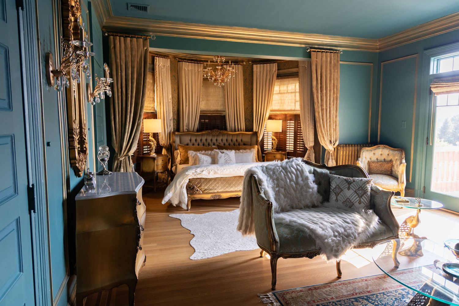 A panoramic view of an elegant bedroom with blue walls, white furniture, and ornate decor in a classic hotel setting.