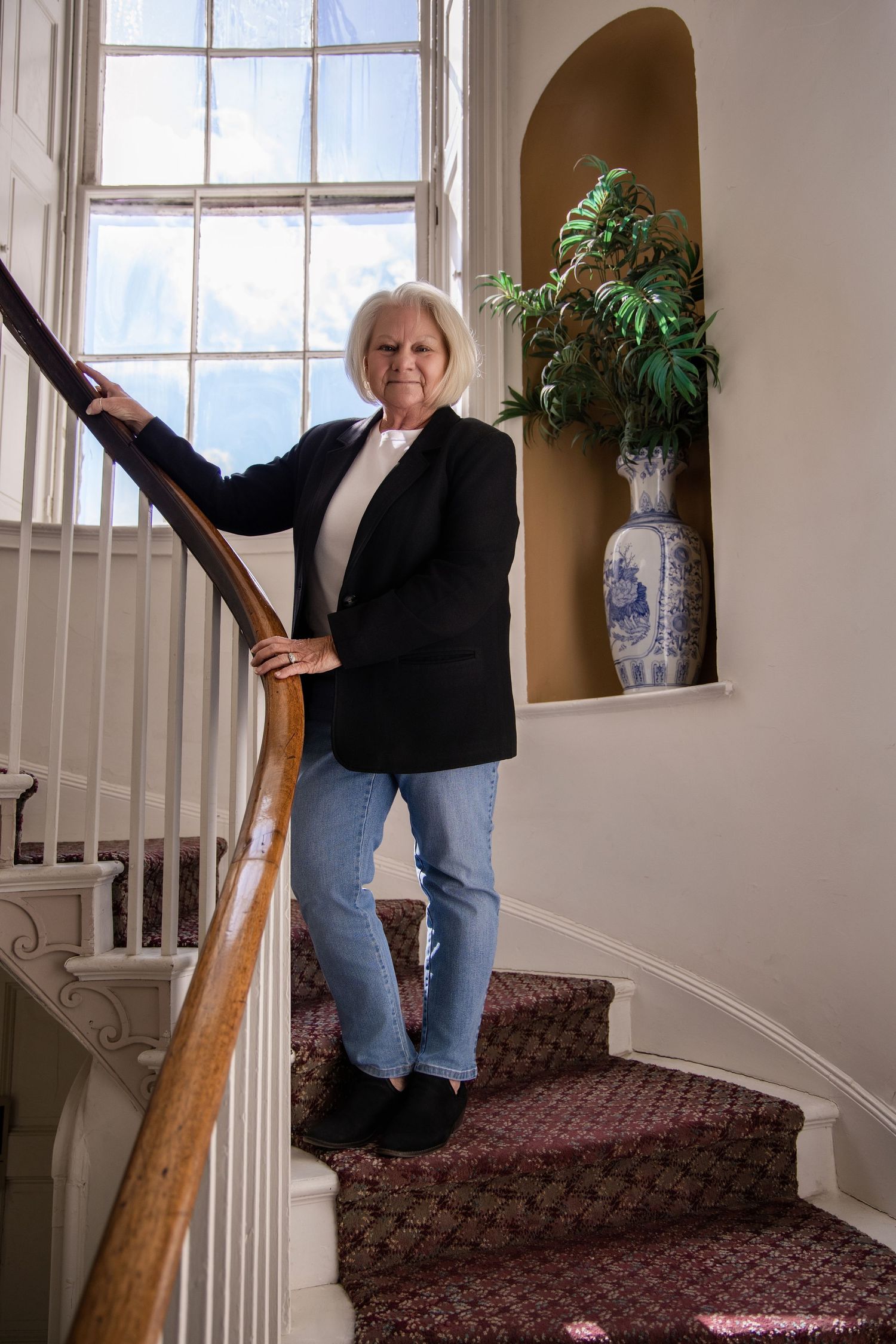Casual business portrait of woman in black blazer and jeans on carpeted staircase.