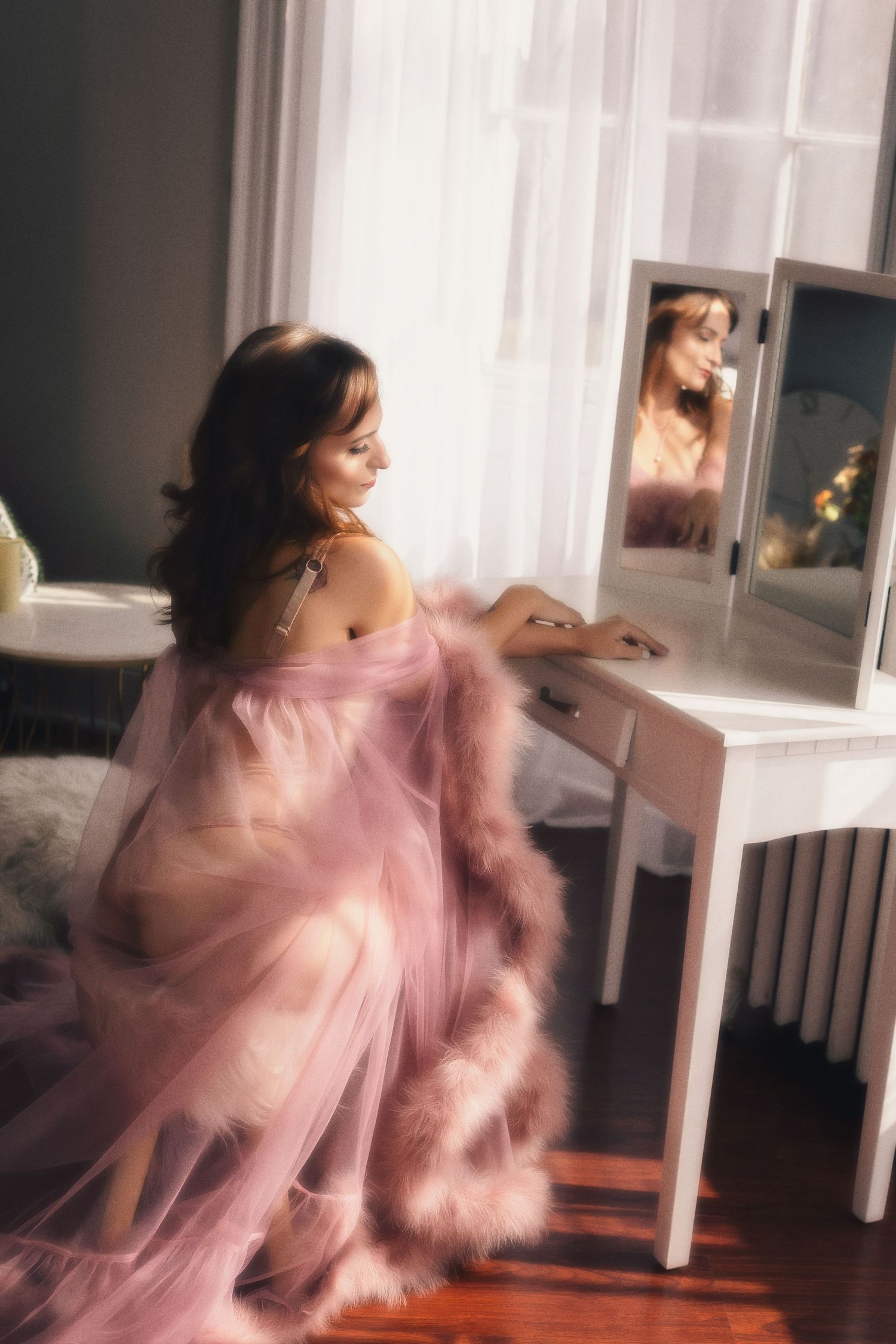 A figure in a flowing pink dress and tulle fabric creates ethereal motion blur while dancing in a sunlit room.
