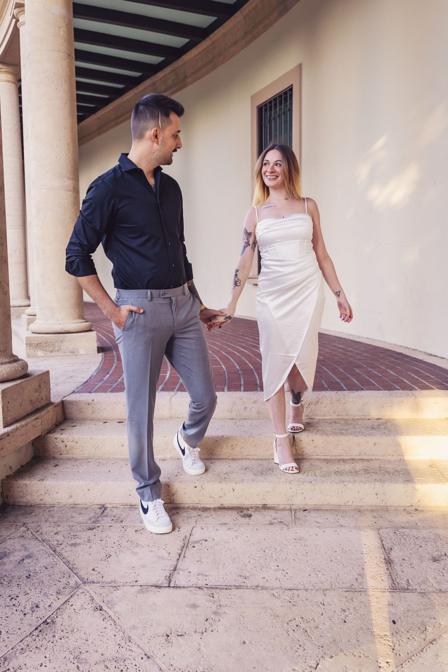 A couple in contrasting outfits demonstrating step sequences in a dance class under a covered walkway.