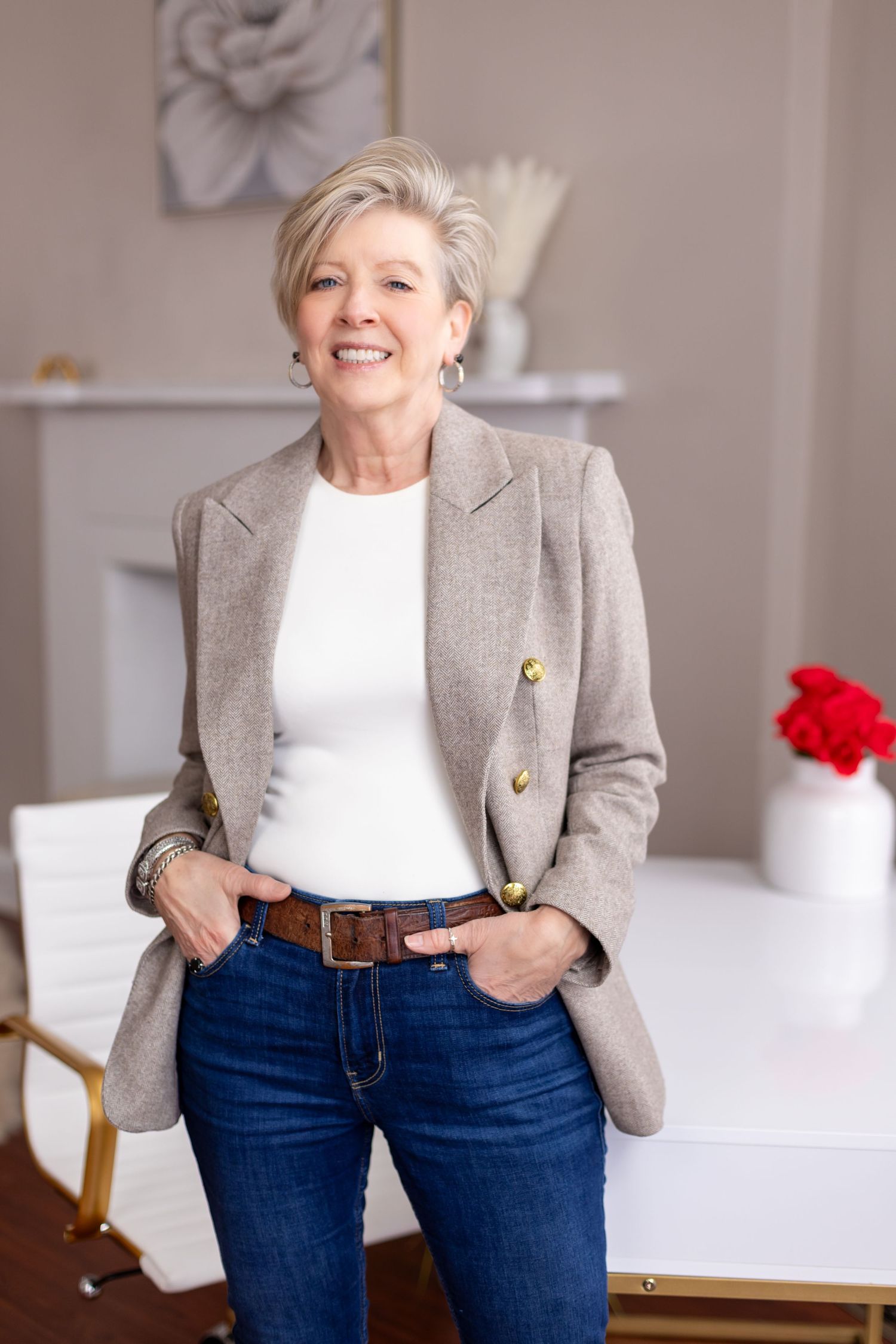 Stylish woman wearing grey blazer and jeans poses casually in modern interior.