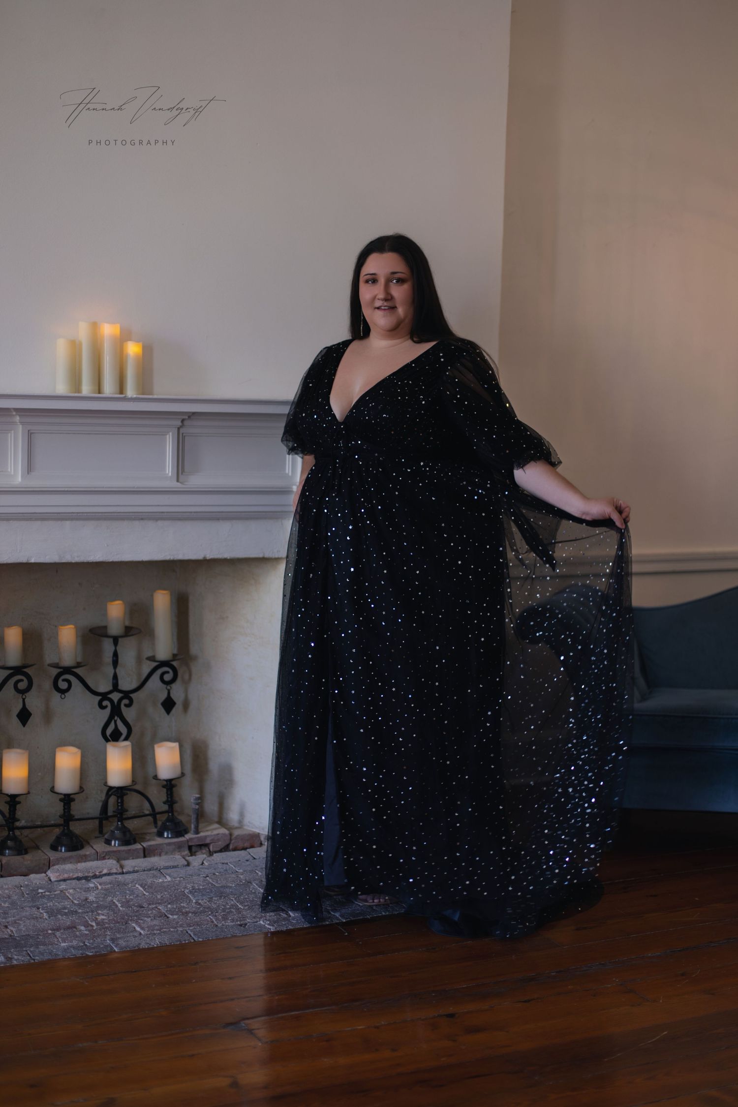 Person wearing sparkly black evening gown poses elegantly near fireplace with lit candles.