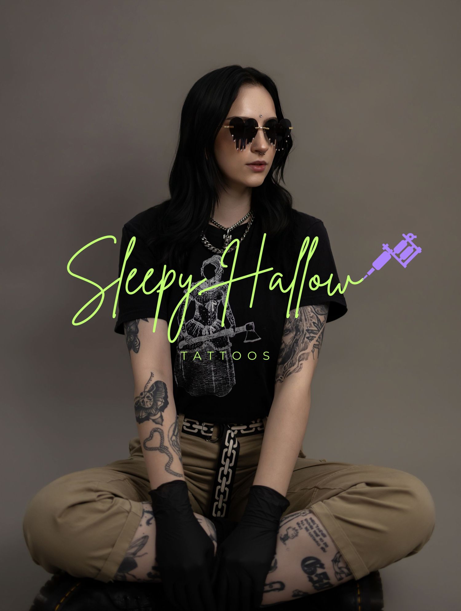 Tattooed female tattoo artist in black gloves poses with Sleepy Hallow Tattoos branding overlay.