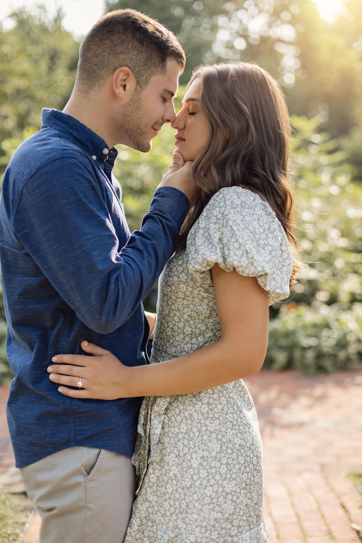 A couple shares tender romantic moments in a sunlit garden setting while wearing casual blue and white attire.