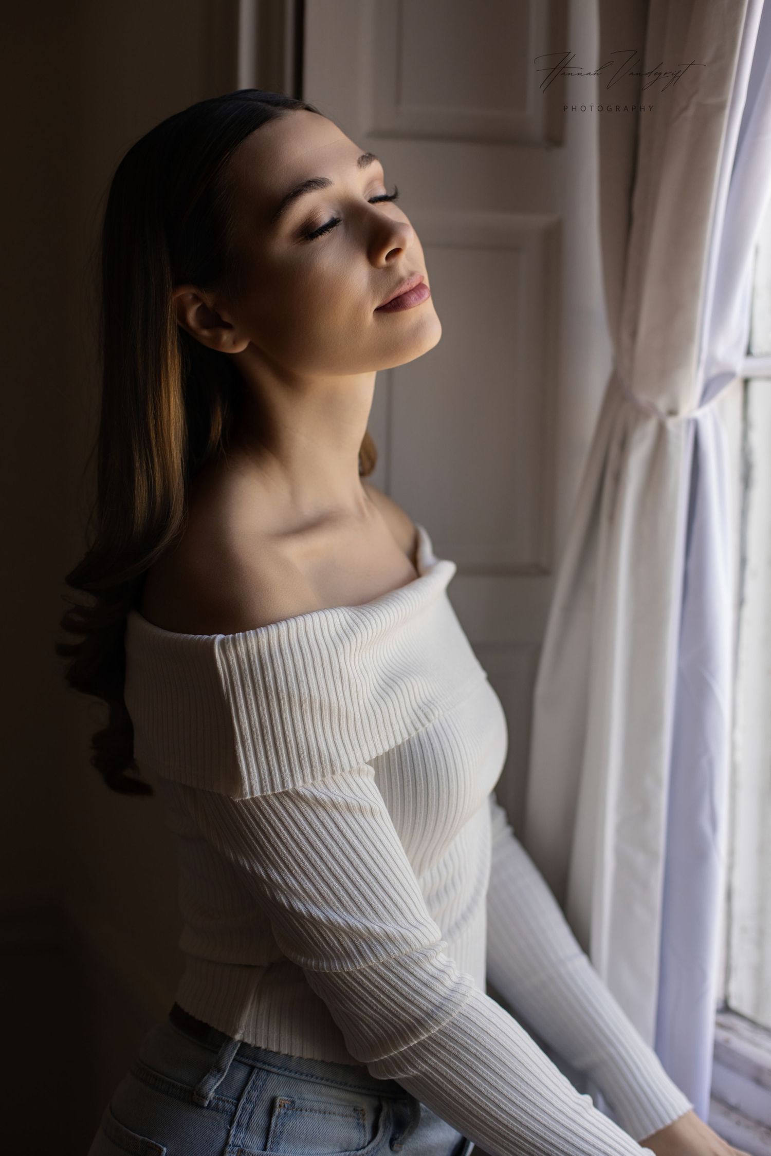 Dramatic portrait of person in white turtleneck sweater by window in natural light.
