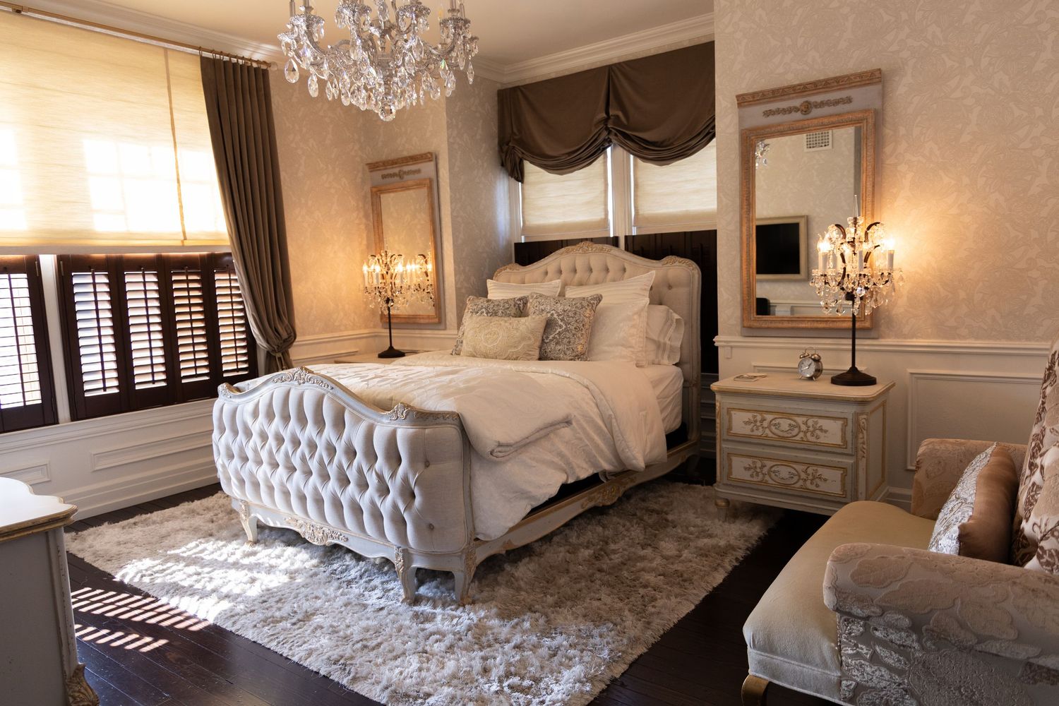 Luxurious bedroom interior with crystal chandelier, tufted headboard, and elegant neutral decor in beige and silver tones.
