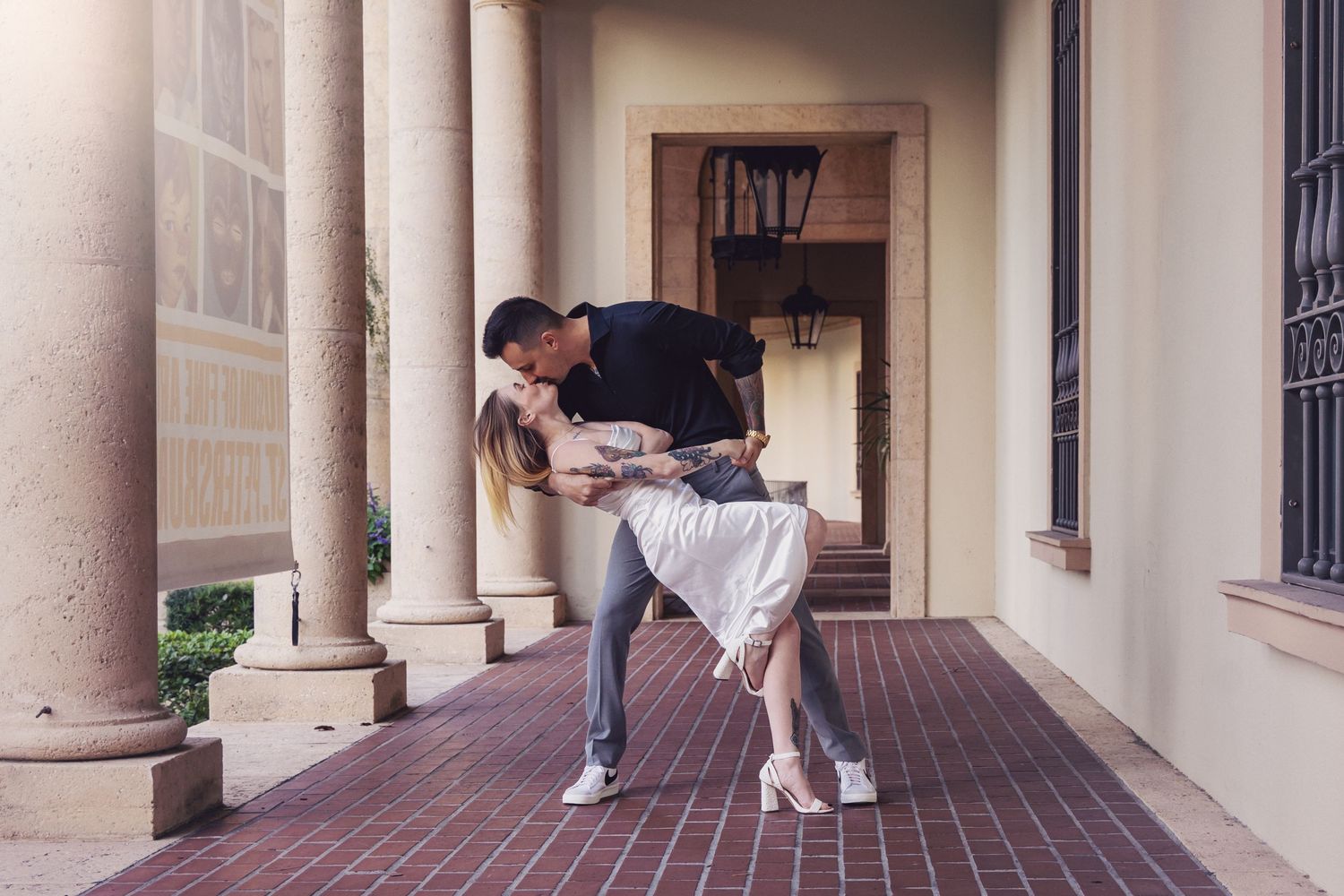 A romantic couple shares an intimate dip pose on an outdoor porch with architectural columns.