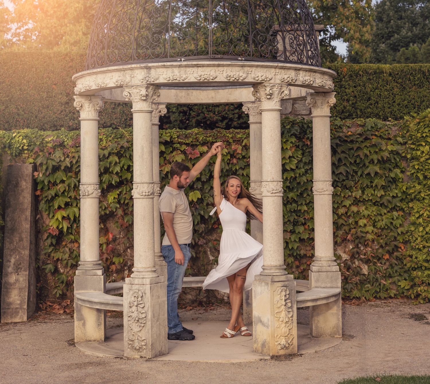 Two people dancing together under an ornate stone gazebo surrounded by green ivy at sunset.