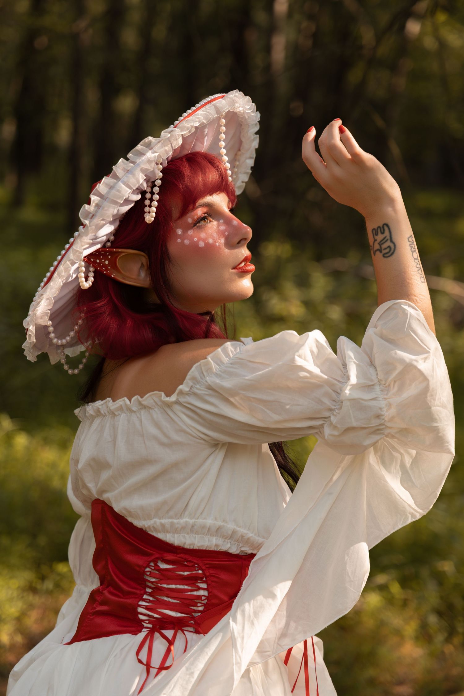 Woman in white off-shoulder dress with red corset and pearl hat poses in forest, fantasy cosplay costume.