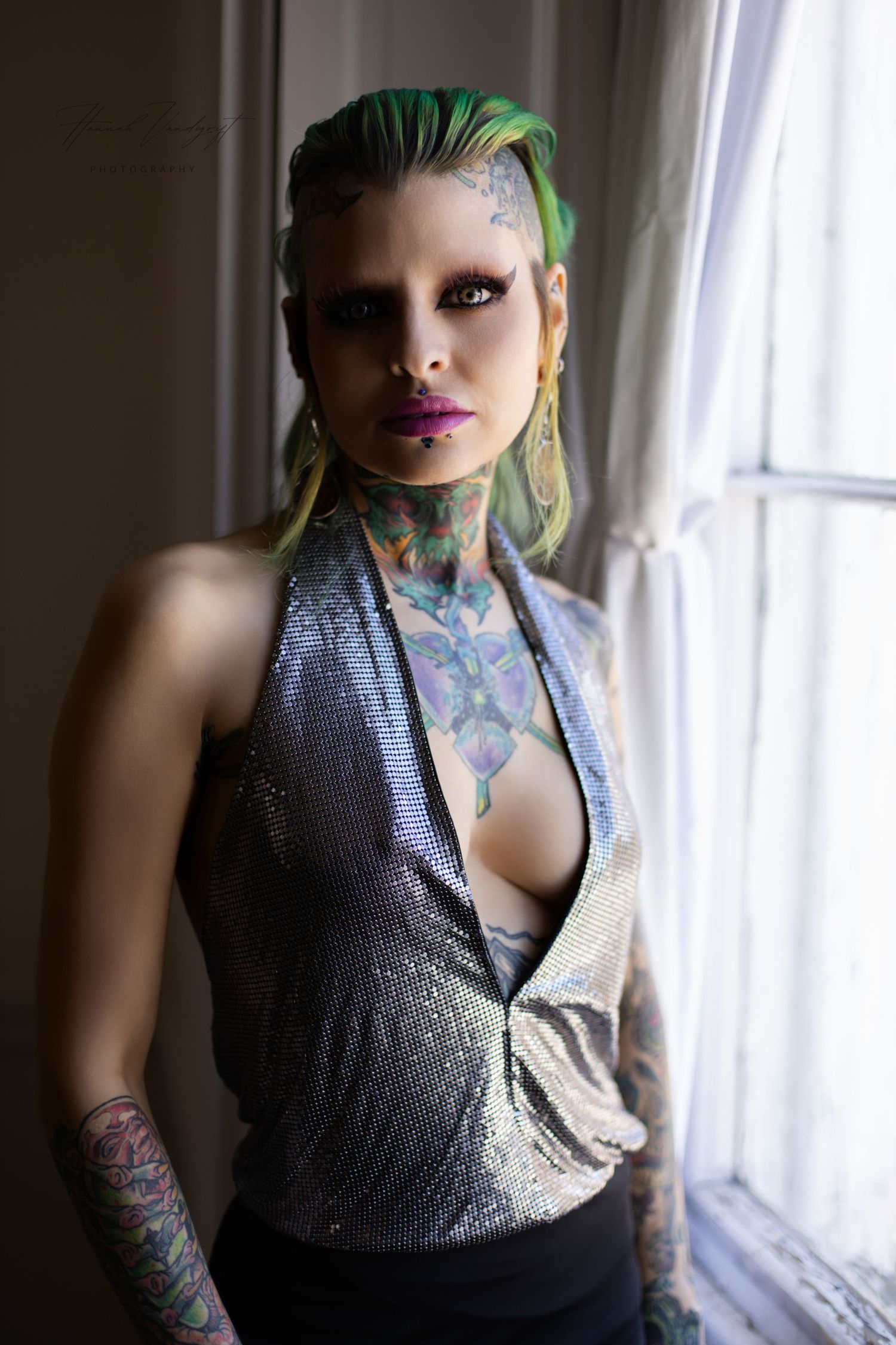 Portrait featuring green hair and tattoos in moody window lighting.