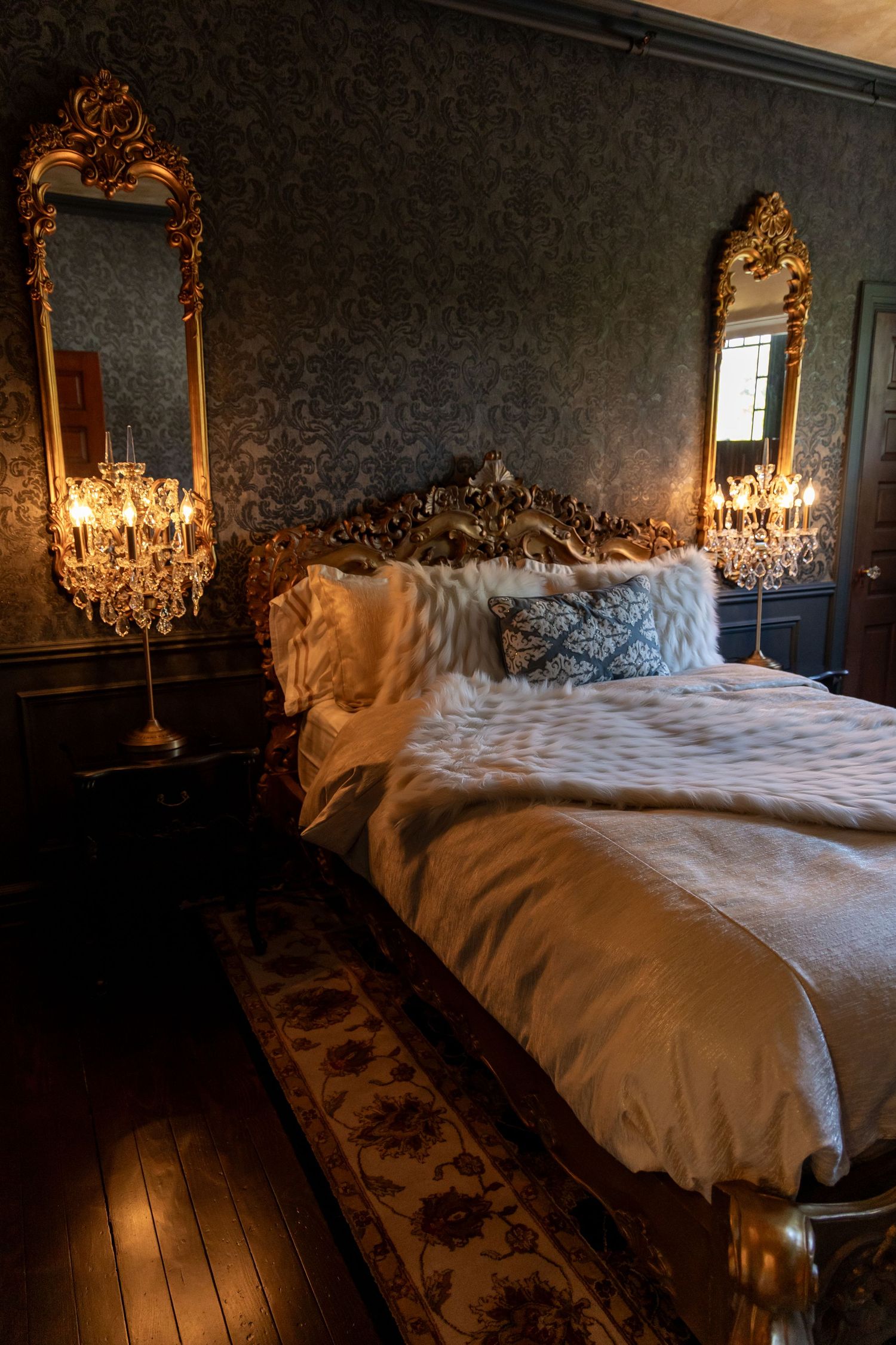 Elegant bedroom with crystal chandelier illuminating a white bed against dark damask wallpaper in vintage style.
