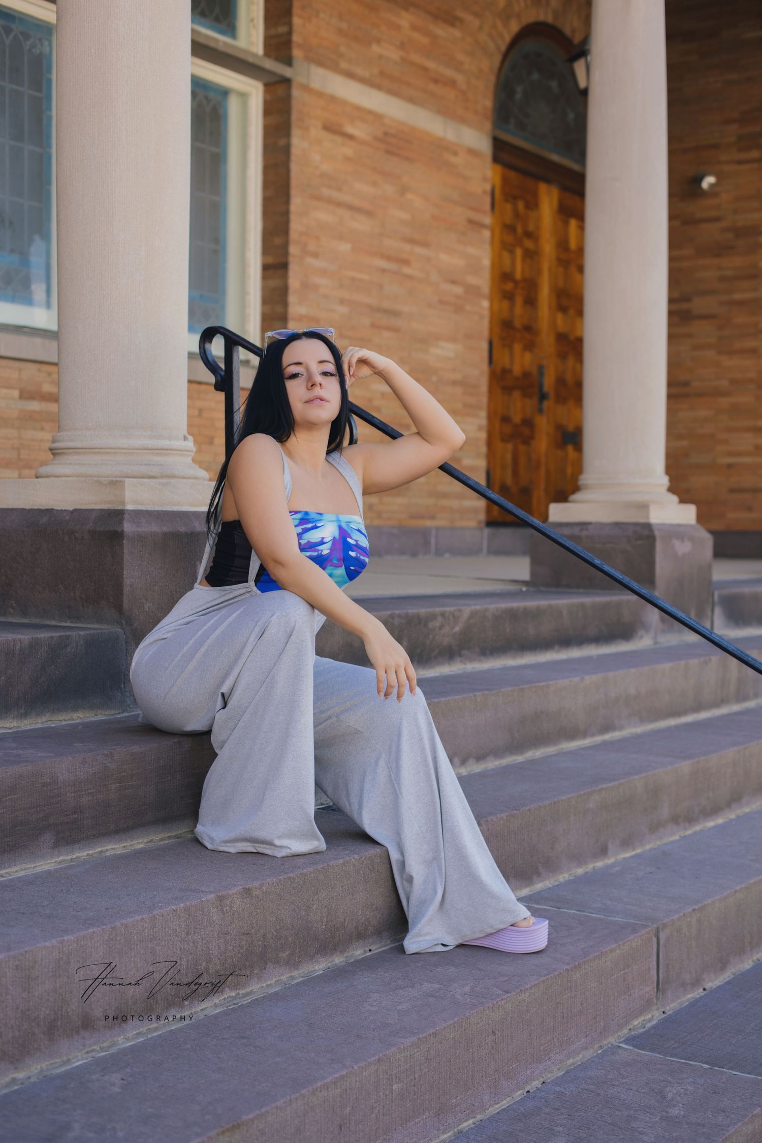 Someone in ballet attire and pointe shoes poses gracefully on concrete steps outside a brick building.