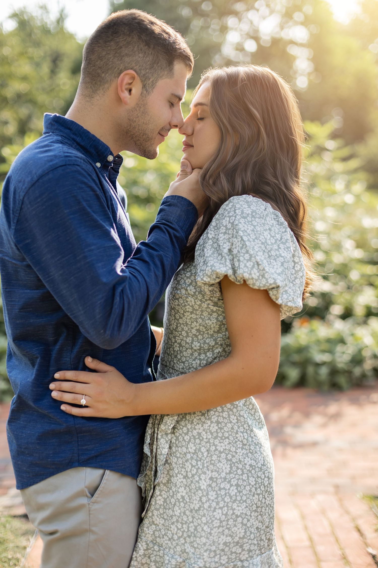 A romantic couple embraces in a sunlit garden setting, sharing an intimate moment on a brick pathway.