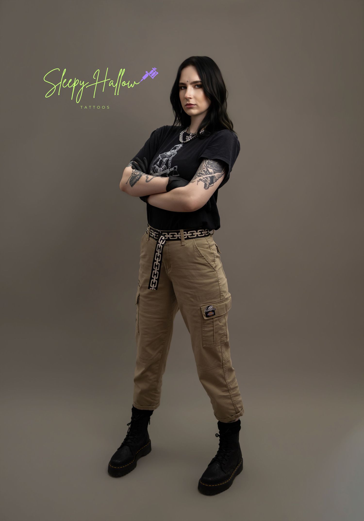 Tattoo artist in black graphic tee and cargo pants with arm tattoos, posing confidently for Sleepy Hollow Tattoos.