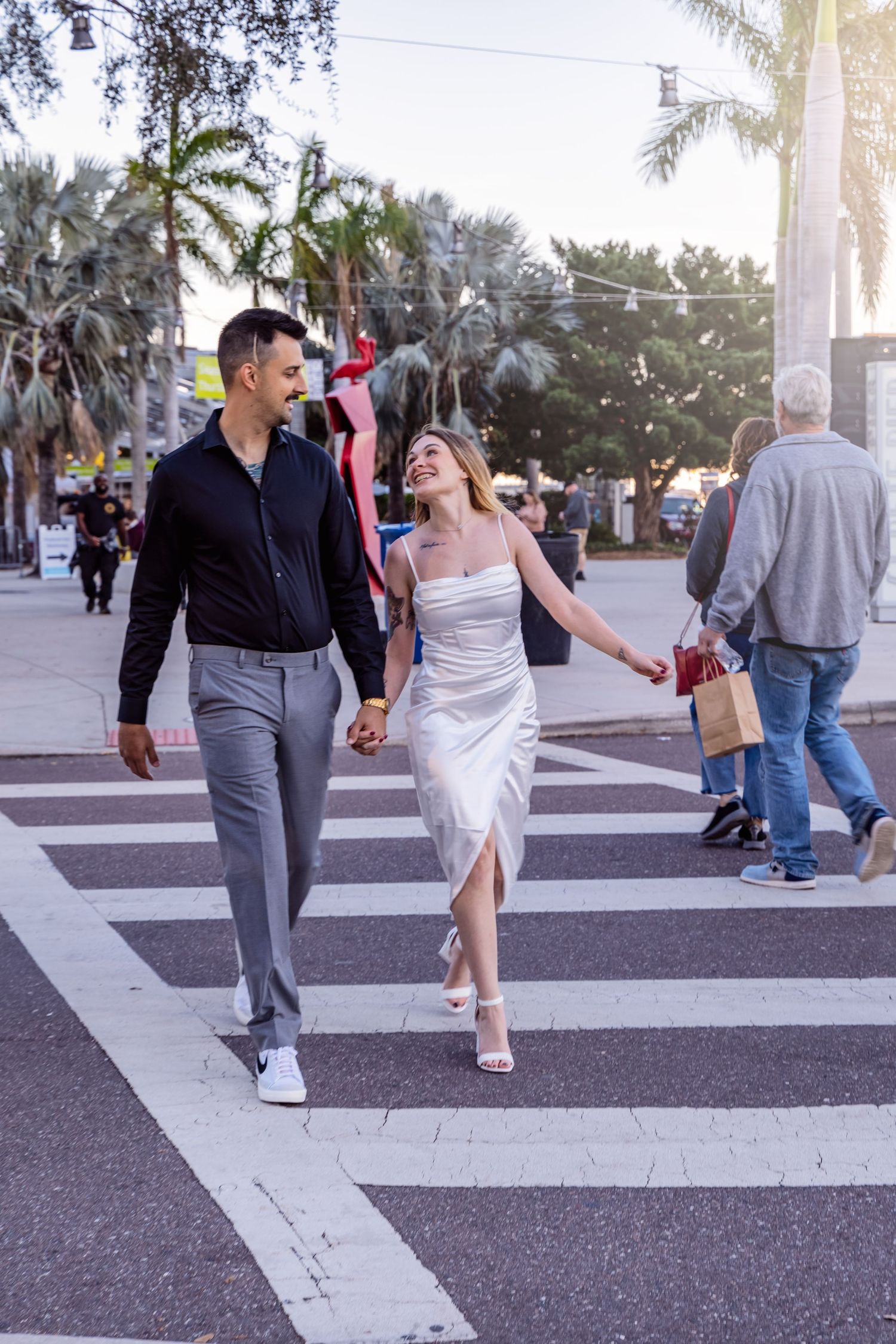 A couple dances playfully across a striped crosswalk on a palm tree-lined street.