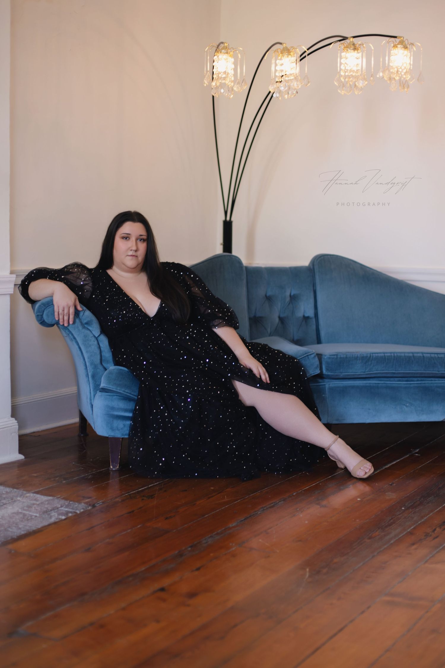 Elegant portrait in sparkly black dress on blue velvet couch with modern floor lamp.